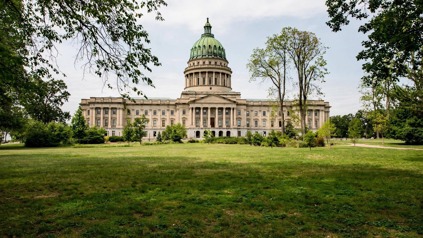 A domed capitol building seen across a grass lawn with trees