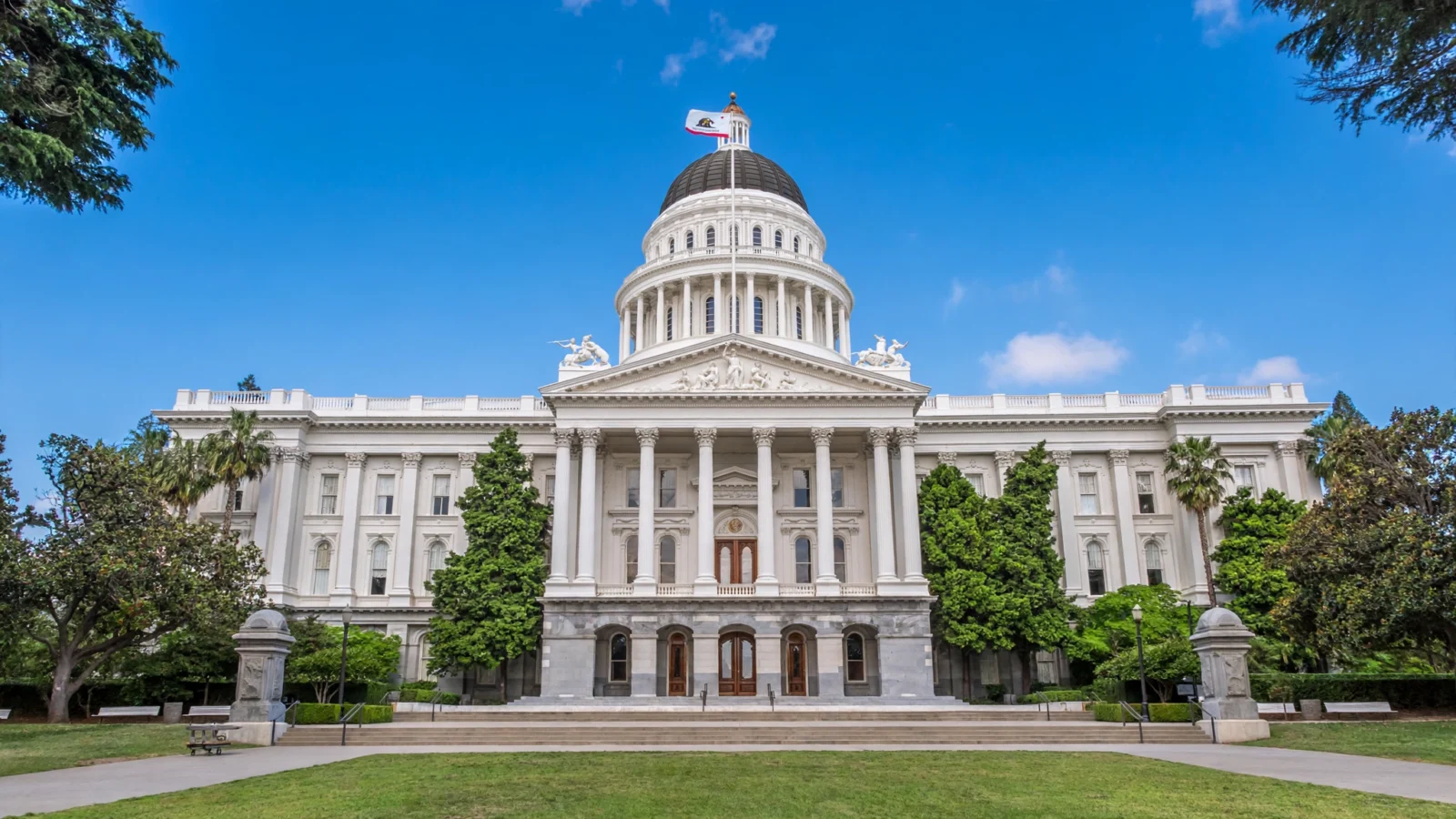 The California State Capitol building in Sacramento, viewed from the west lawn under a clear blue sky.