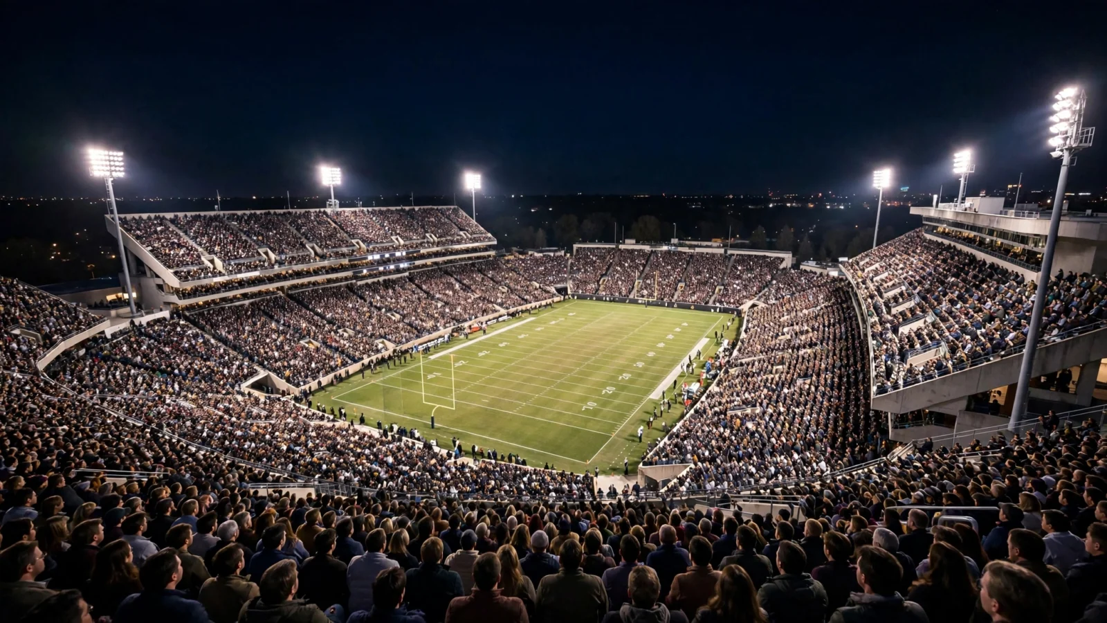 A packed college football stadium lit by floodlights at night.