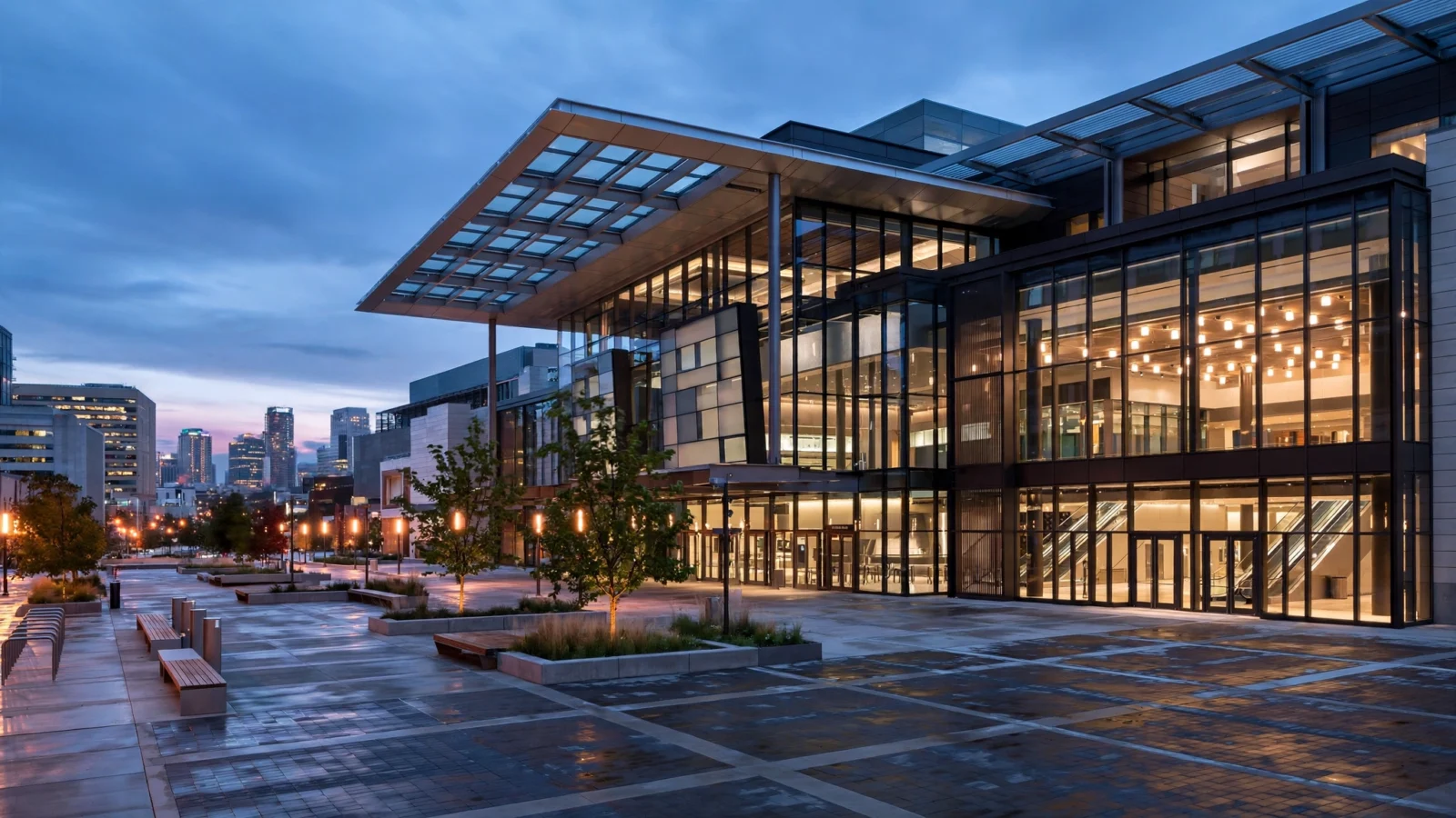 A modern glass convention center with an empty plaza in front at dusk