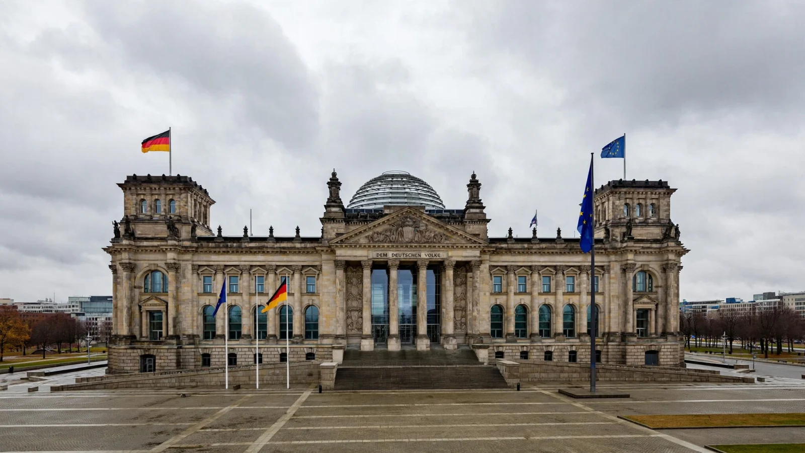 The Reichstag building in Berlin under cloudy skies with German and European Union flags flying