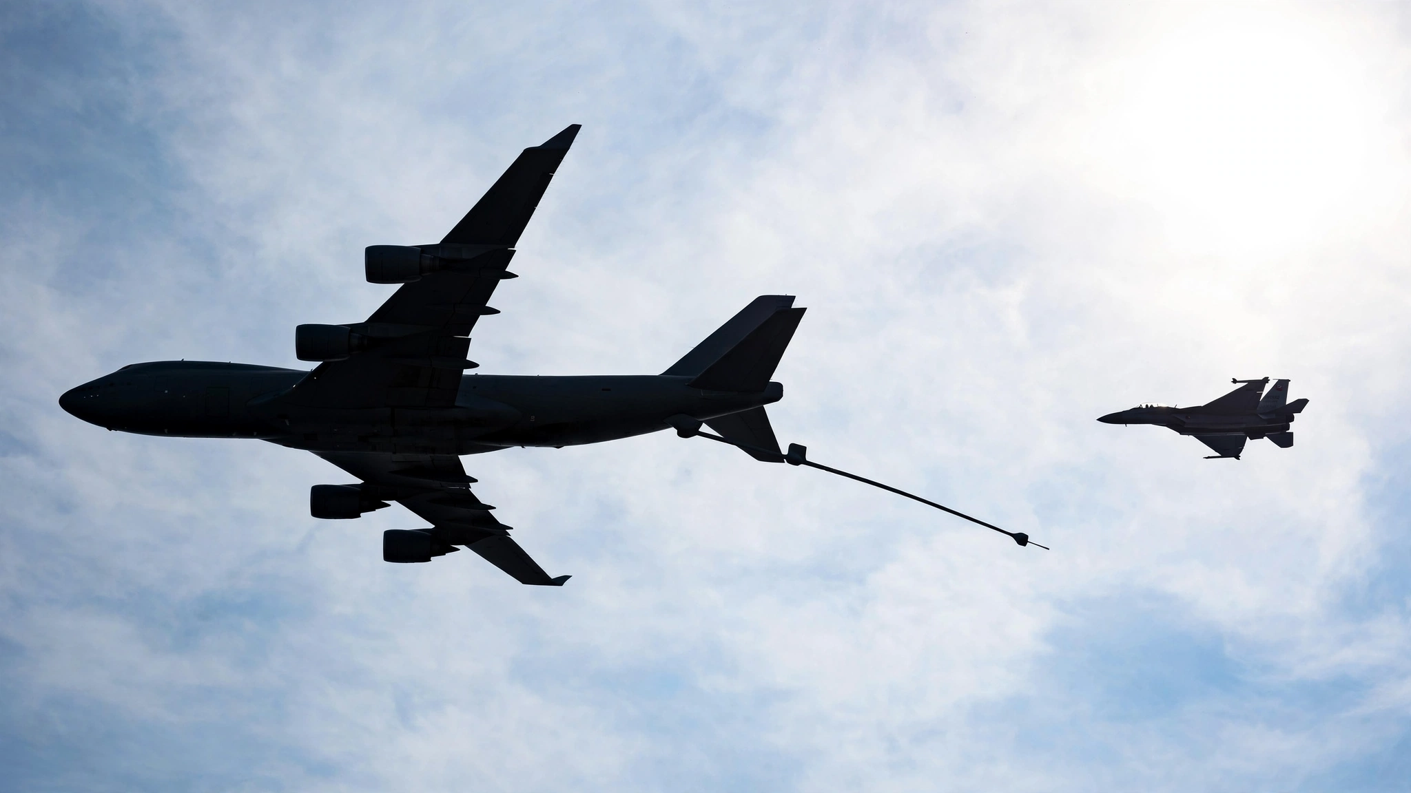 Silhouette of a military aerial refueling tanker flying with its boom extended, with a fighter jet alongside.