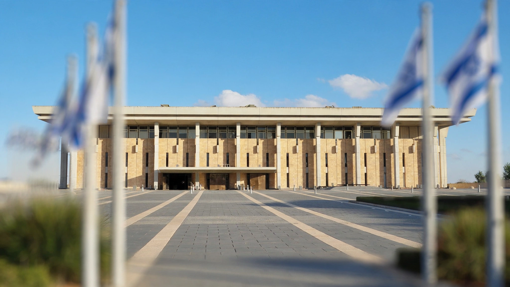Exterior of the Knesset building in Jerusalem with Israeli flags in the foreground.