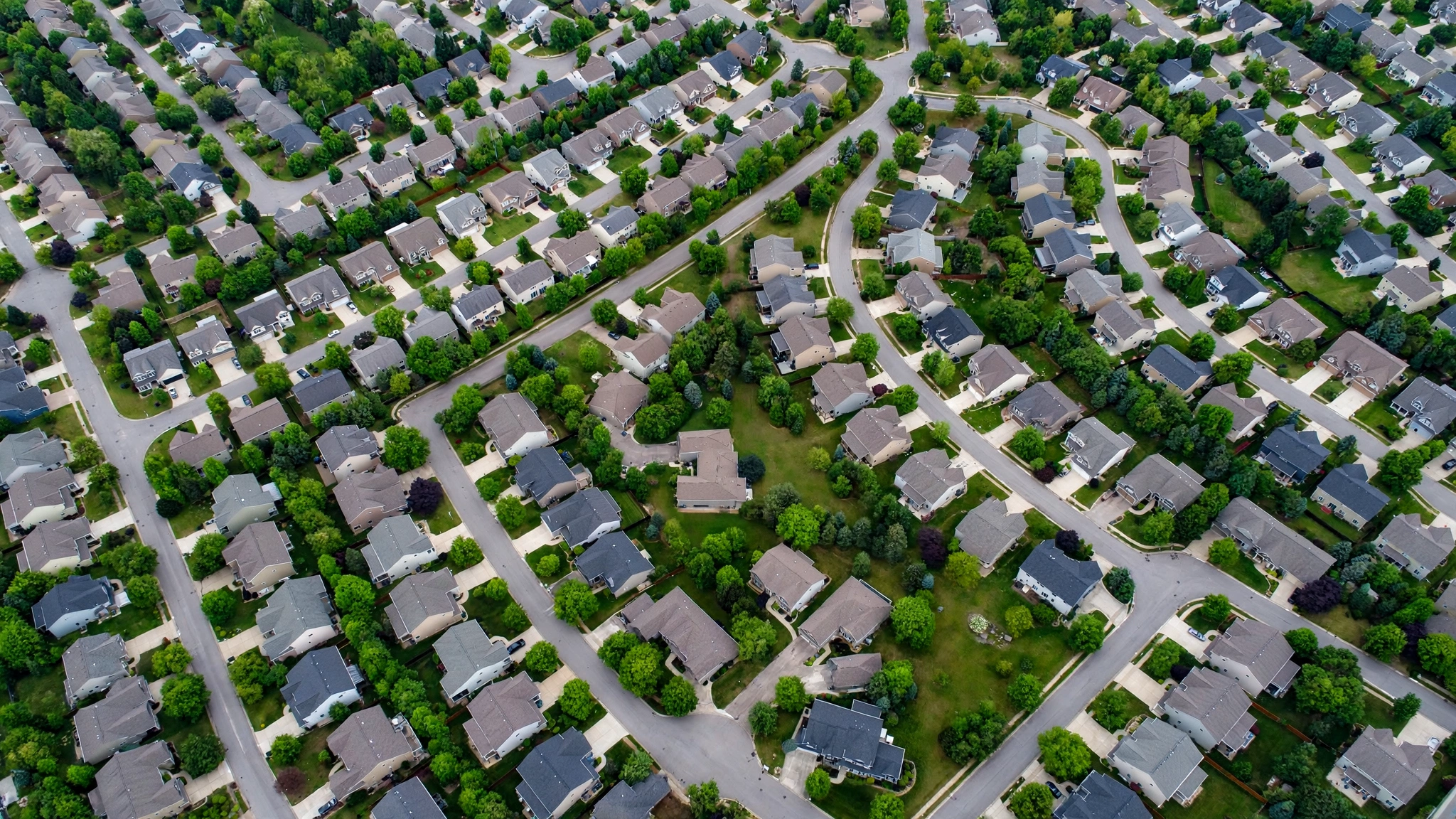 An aerial view of a suburban neighborhood with rows of single-family houses and curving streets.