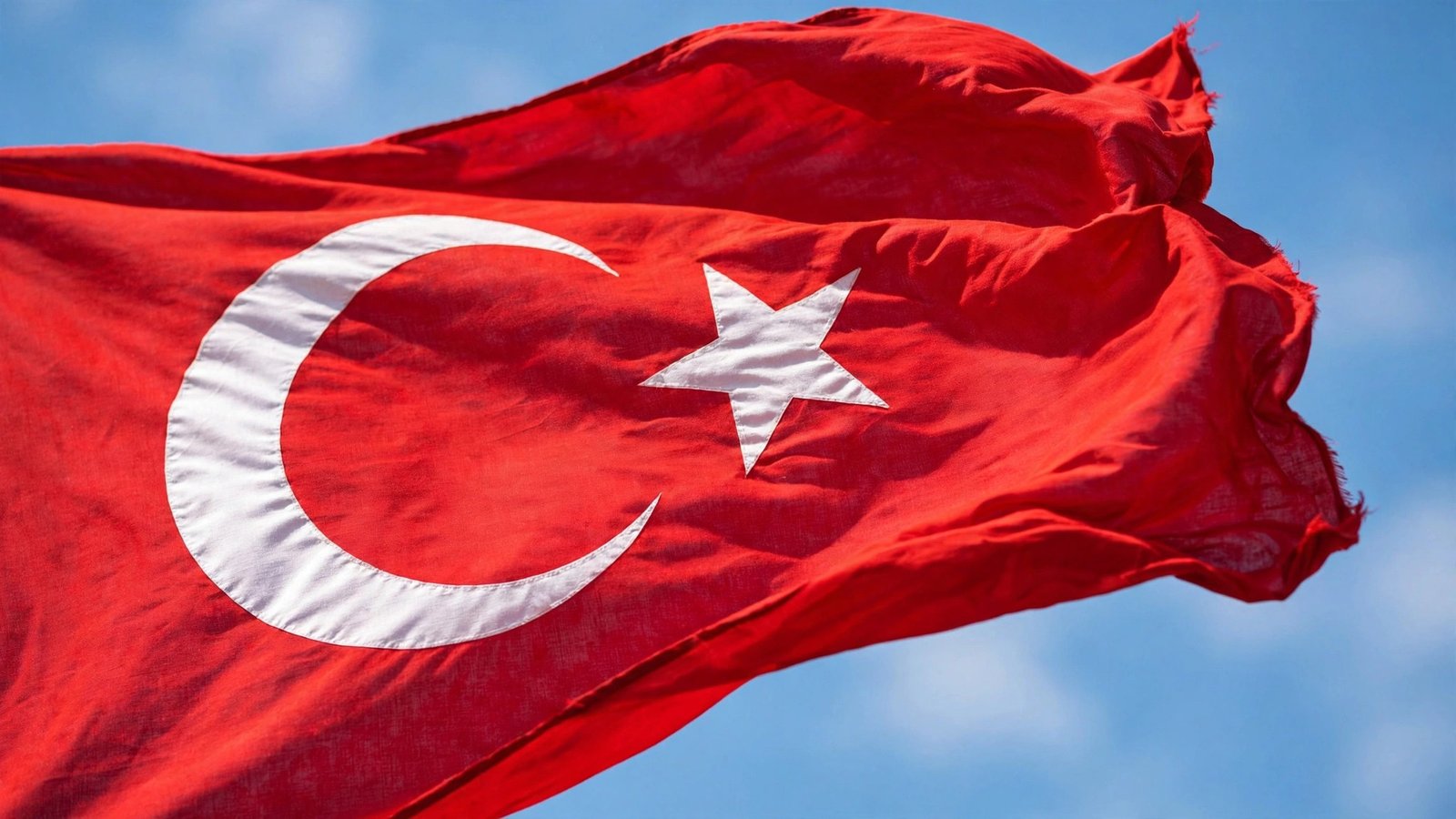 The Turkish national flag waving in the wind against a clear blue sky.