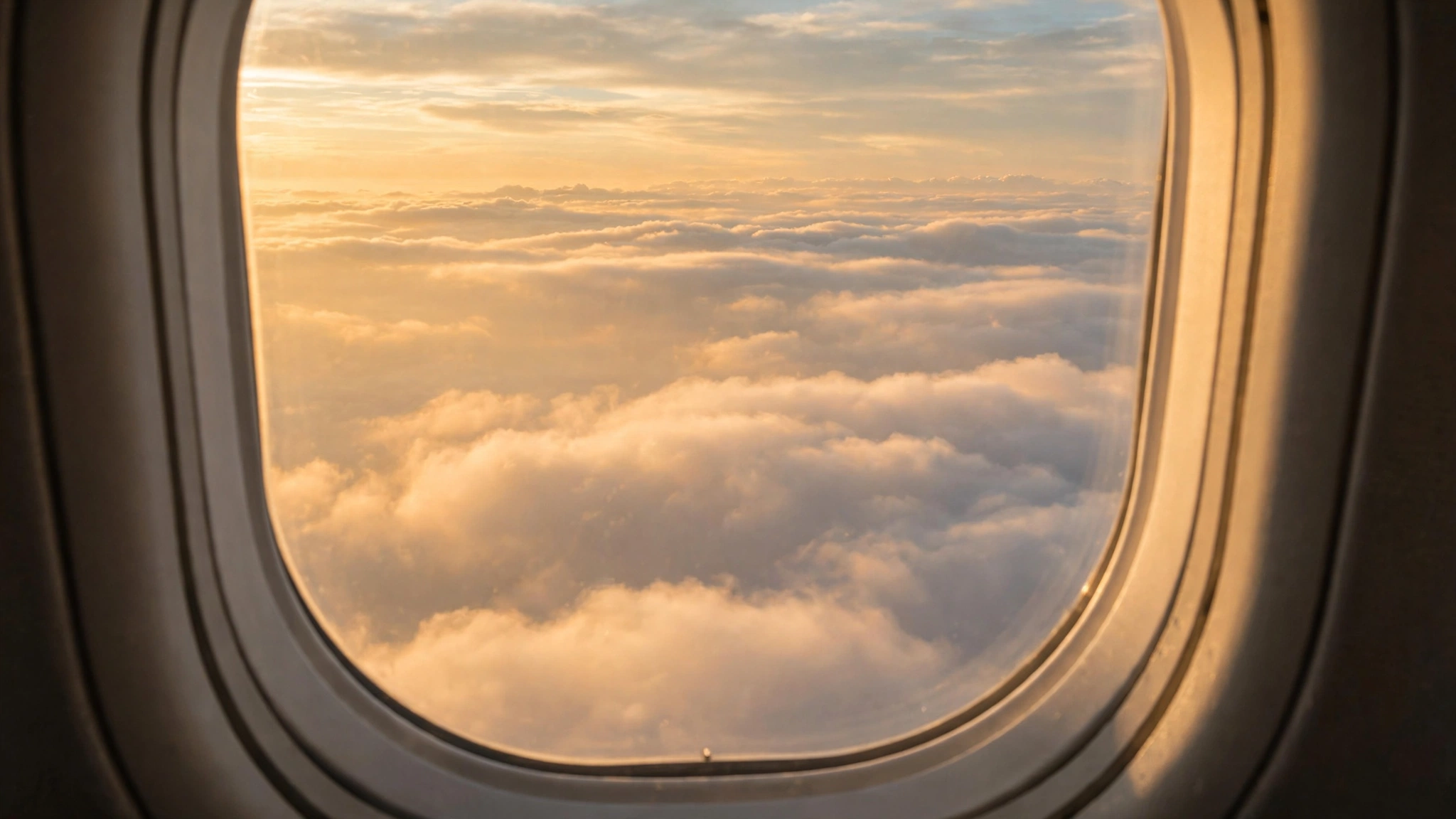 The view through an airplane window showing clouds and a golden morning sky.