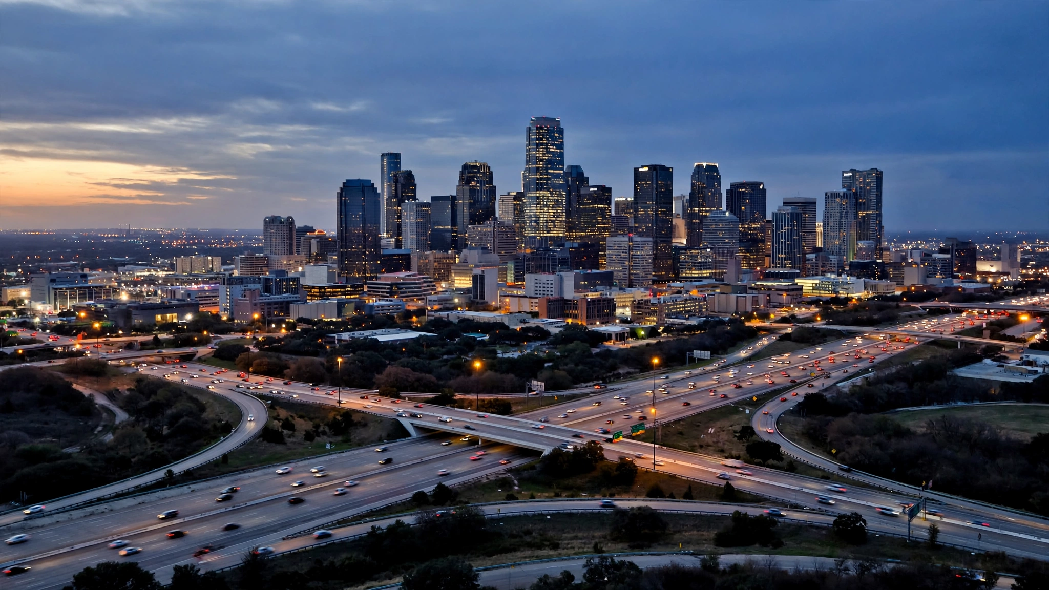 A large city skyline with office towers and busy highways at dusk