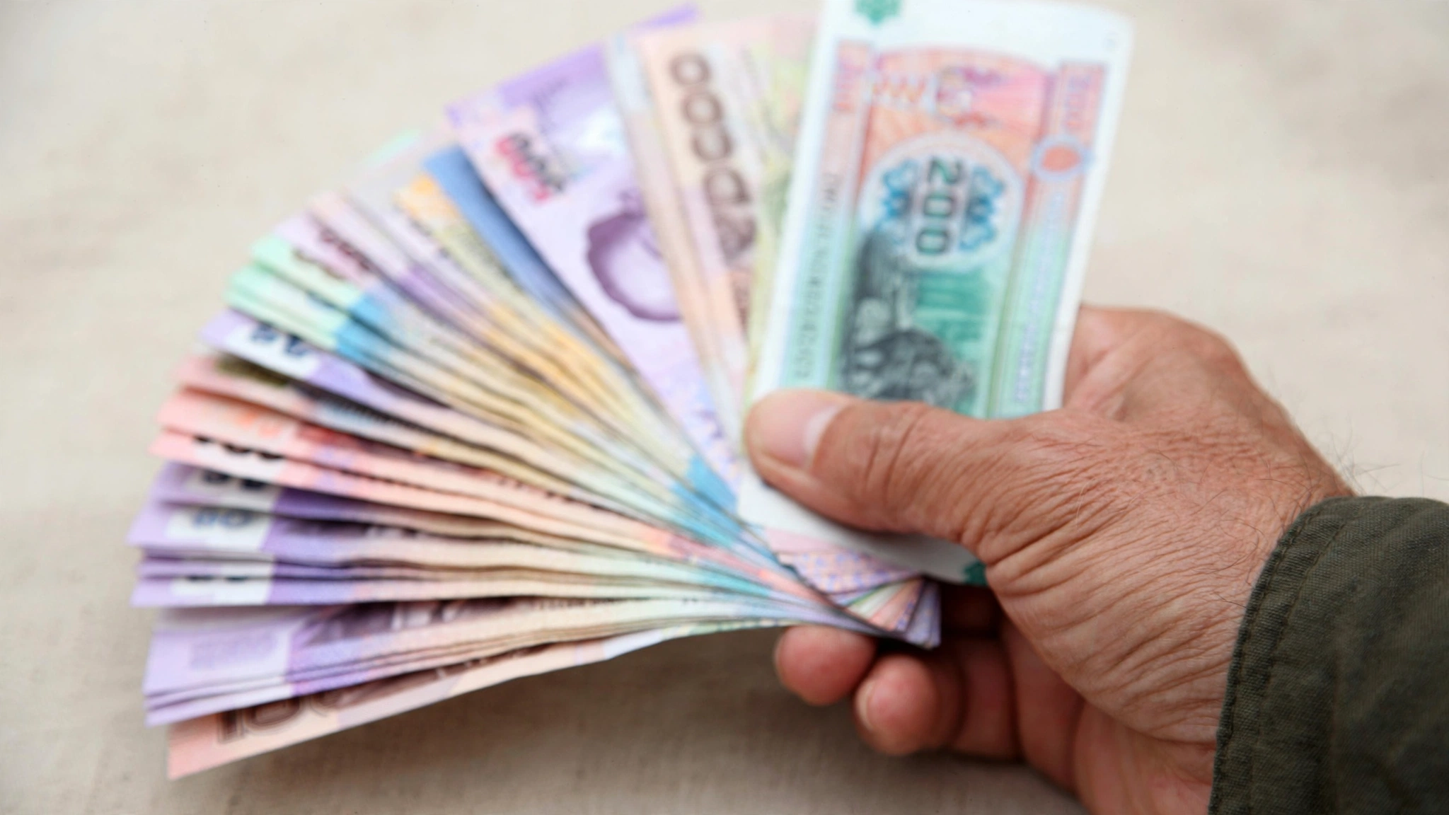 A hand holding a fanned stack of Southeast Asian paper banknotes