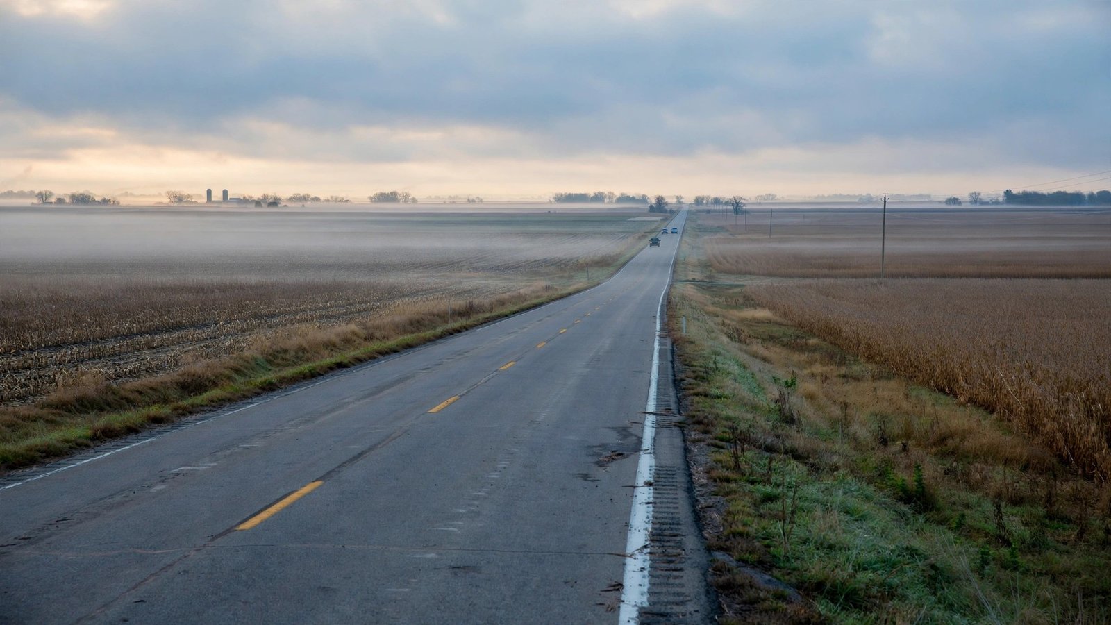A two-lane rural highway through flat farmland at dawn