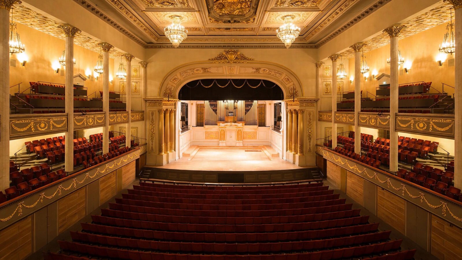 Ornate concert hall interior in Stockholm with rows of empty red seats and a warmly lit stage, where the 2026 Nobel Prize in economics was announced.