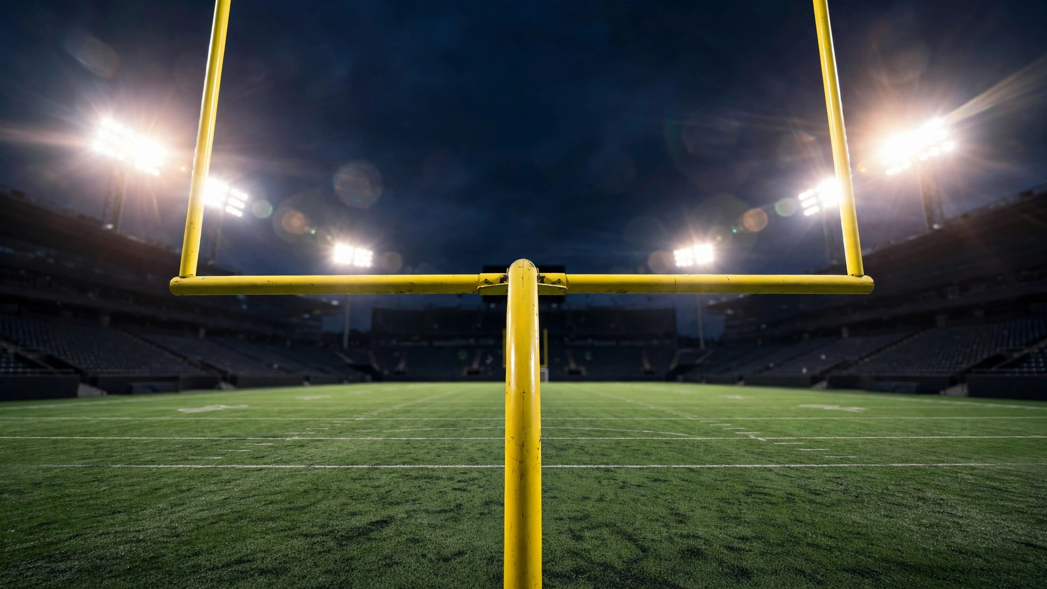 Yellow football goalposts framed against a night sky with stadium floodlights flaring