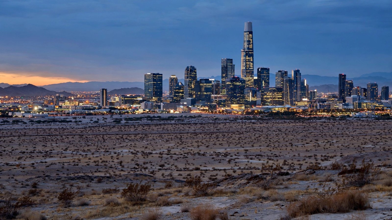 City skyline with tall skyscrapers glowing at dusk above desert outskirts