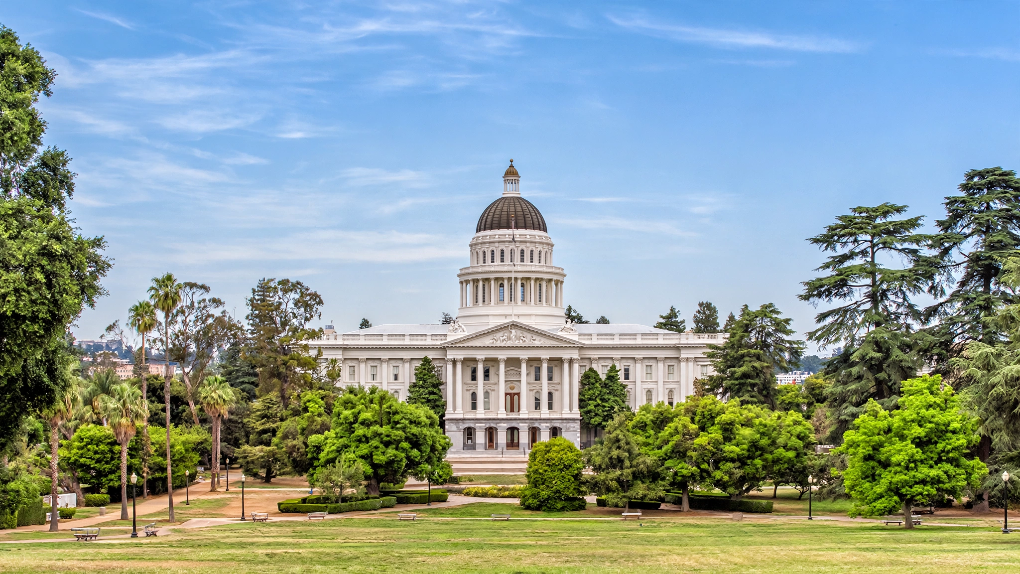 The California State Capitol building in Sacramento surrounded by trees and green lawns.
