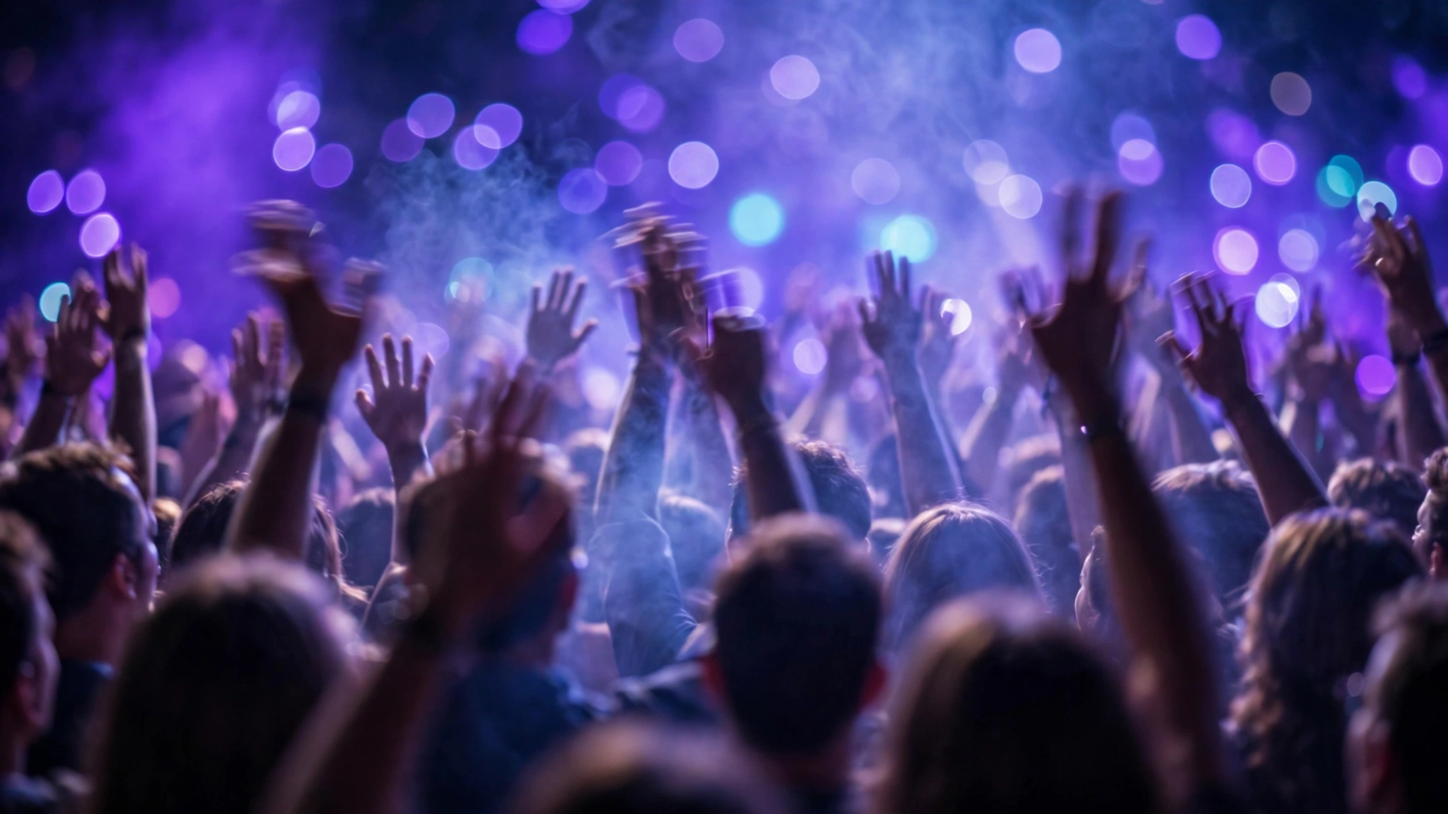 Concertgoers with raised hands under purple and blue stage lights.