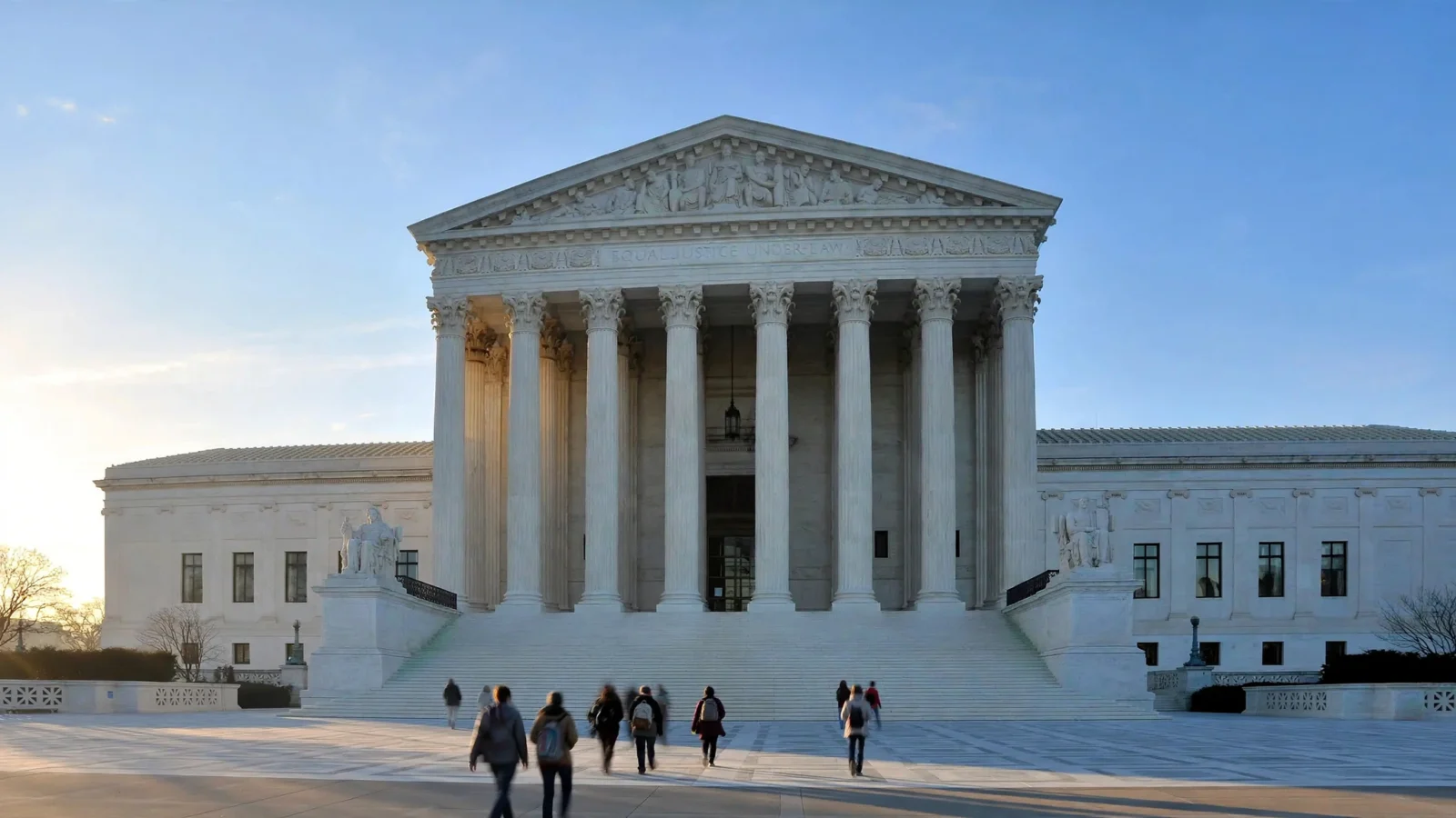 The white marble facade and columns of the United States Supreme Court building in Washington, D.C., in early morning light, with a few indistinct visitors walking toward the steps