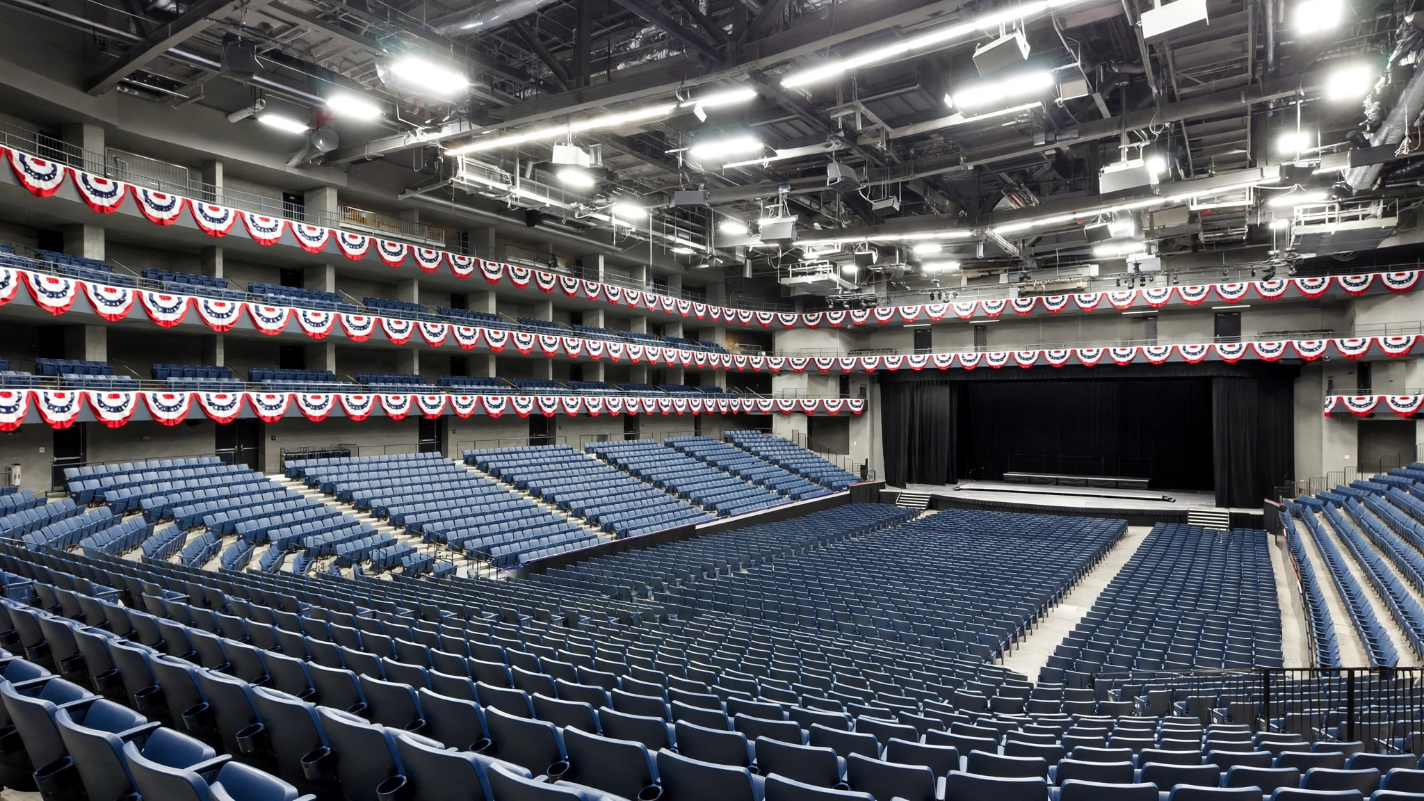 Rows of empty blue arena seats with red, white and blue bunting along the upper levels and an empty stage