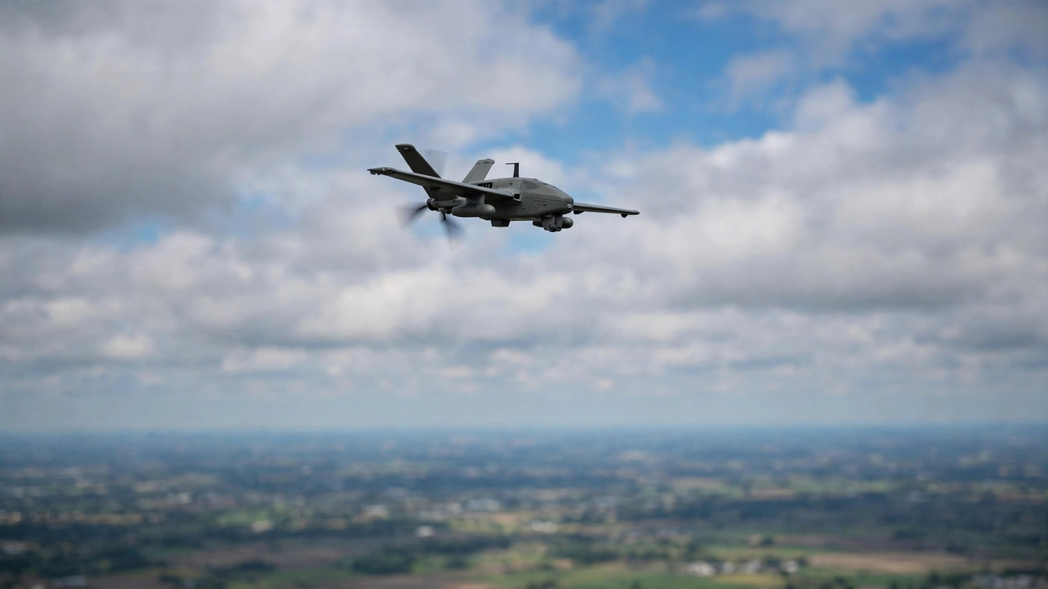 A military-style drone aircraft flying in a cloudy sky over blurred ground below