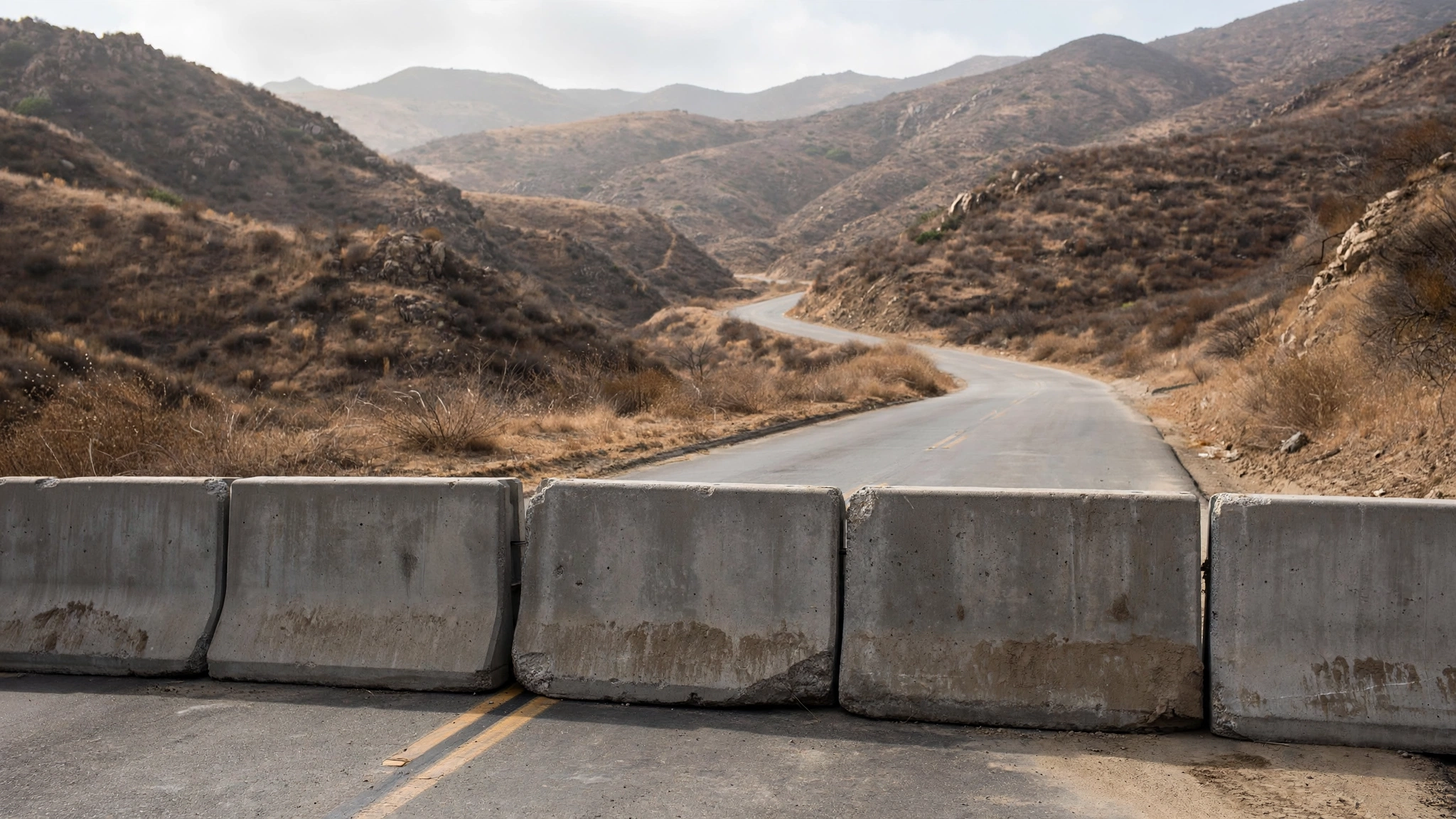 Concrete barriers blocking an empty paved road through dry hills