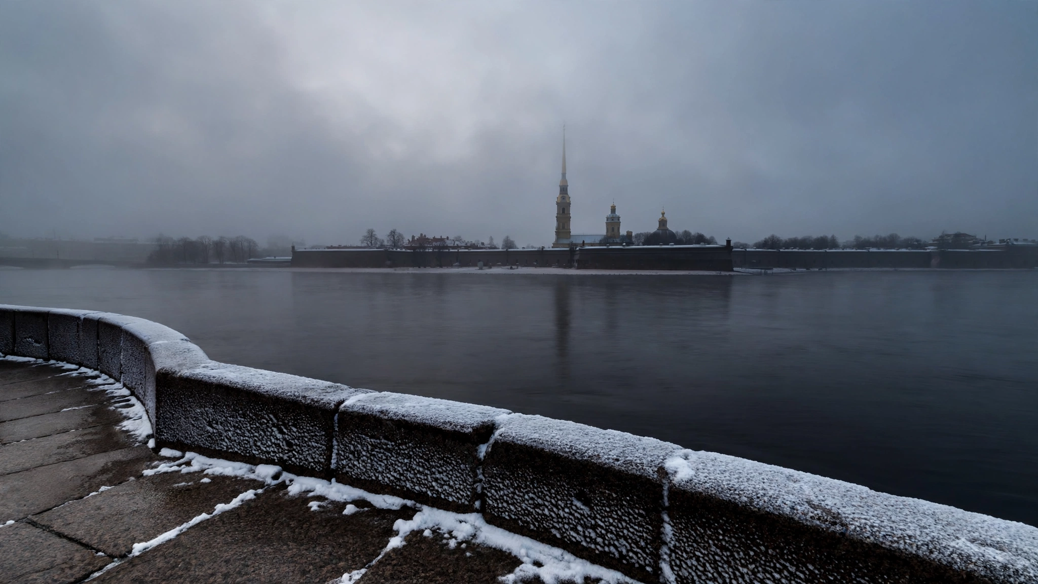 A snow-dusted stone embankment along the Neva River in St. Petersburg, with the Peter and Paul Fortress across the water on a gray morning