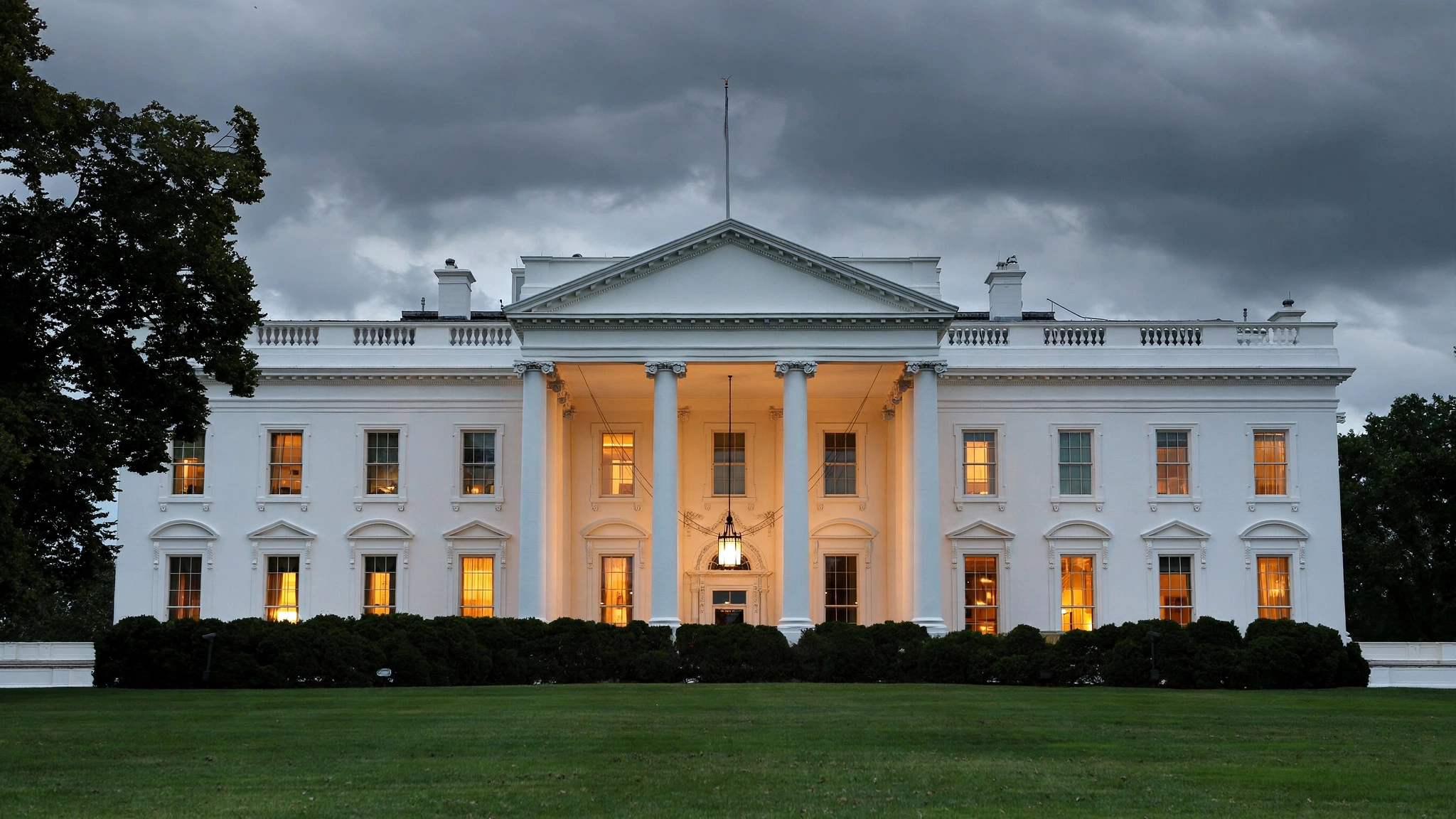 The White House north facade at dusk with warm lights in the windows.