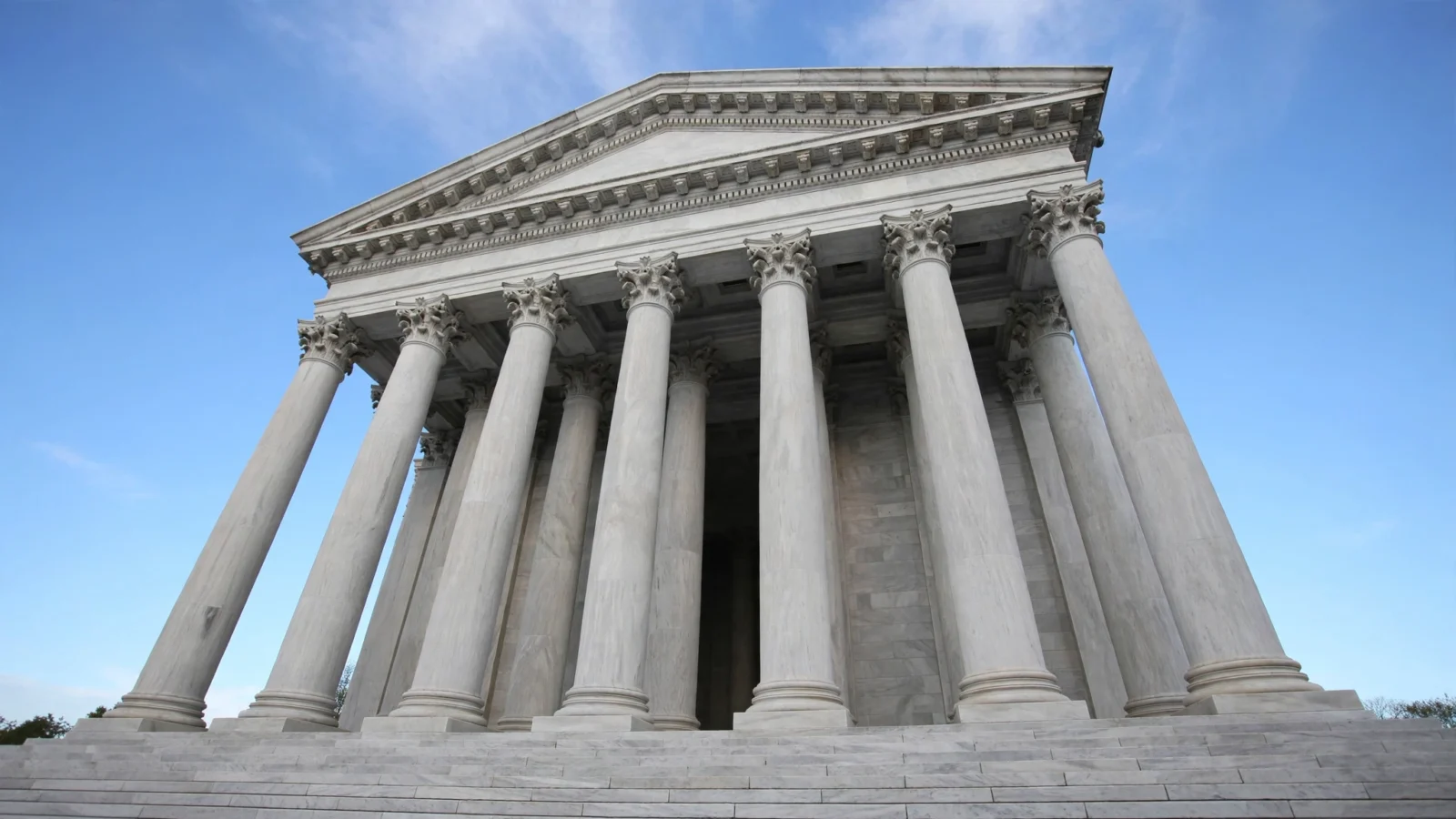 A marble courthouse facade with tall columns photographed from below against a blue sky