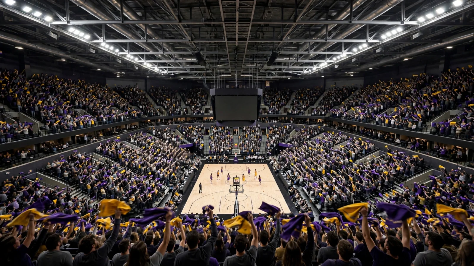 Wide view of a basketball arena full of fans waving purple and gold rally towels above a court