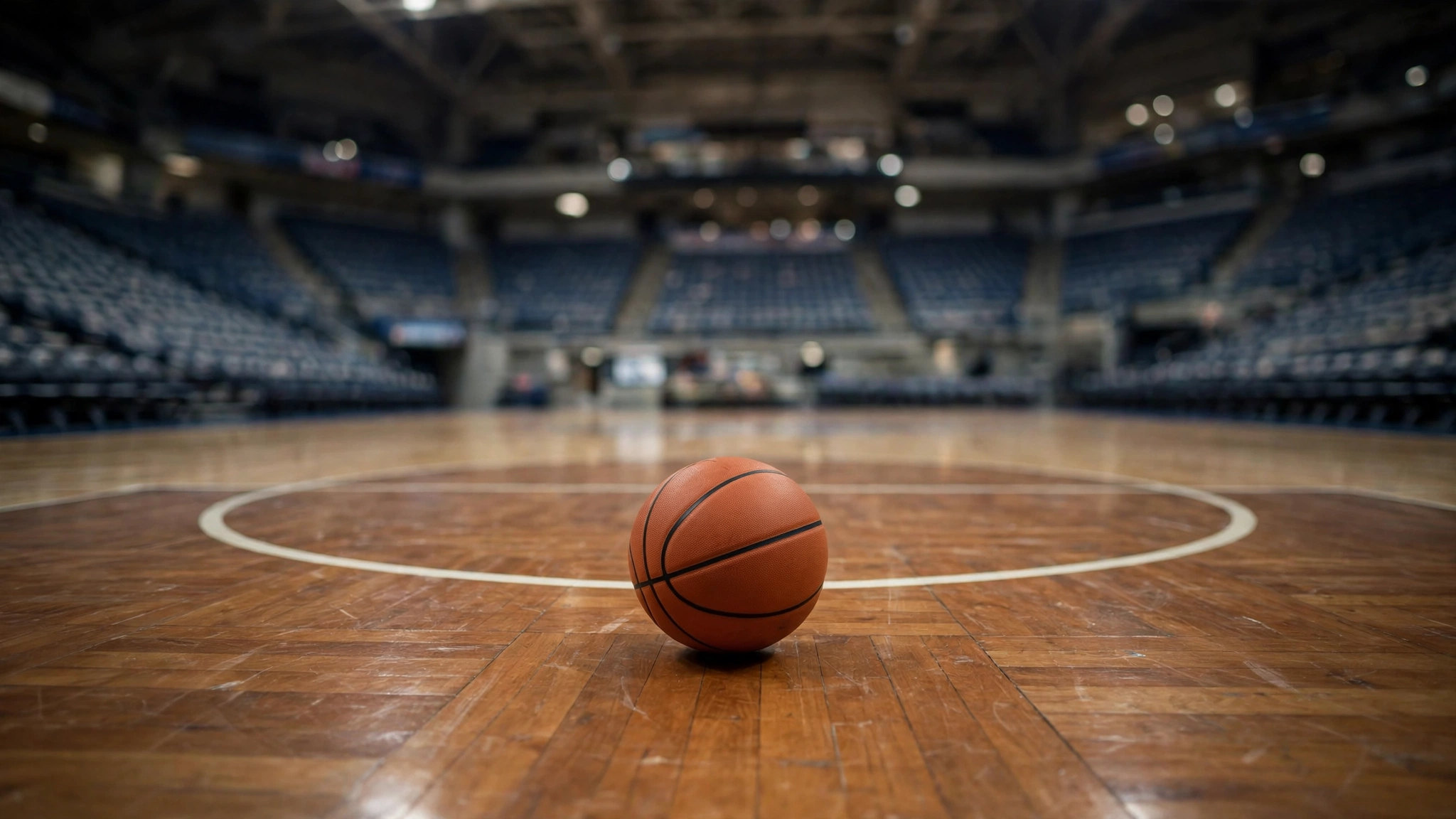 A basketball resting on a polished wooden court in an empty arena