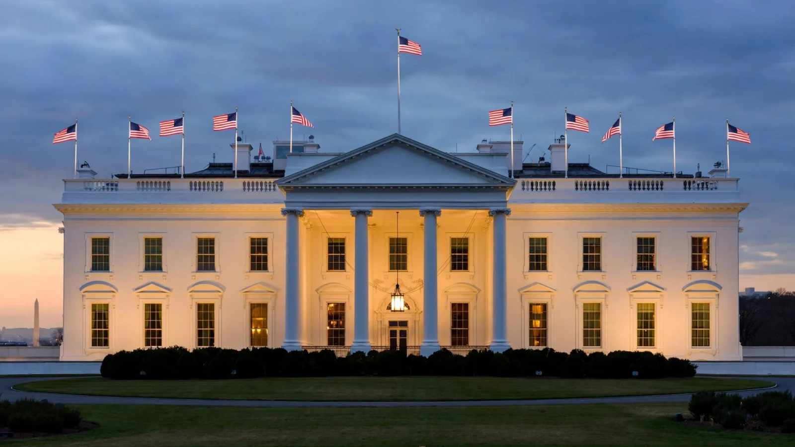 The White House lit up at dusk with American flags flying from the roof