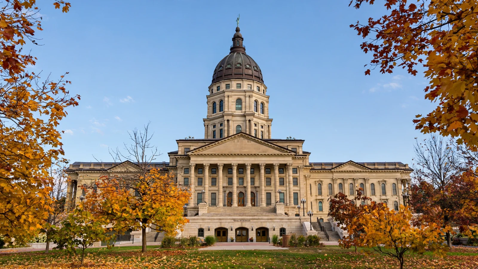 The Kansas State Capitol building in Topeka framed by trees with autumn leaves
