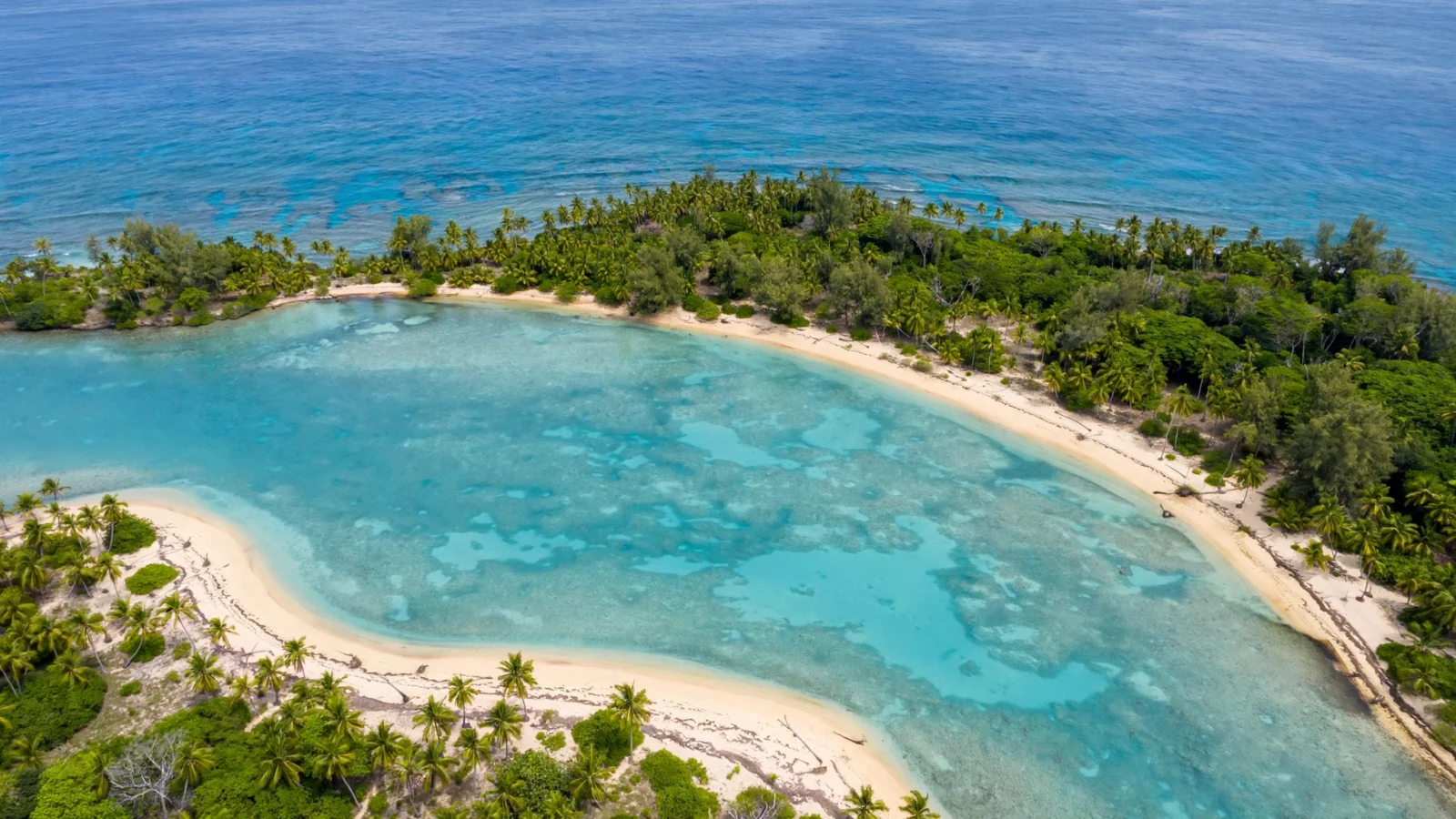 Aerial view of a tropical Pacific island coastline with turquoise water, a sandy beach, and palm trees