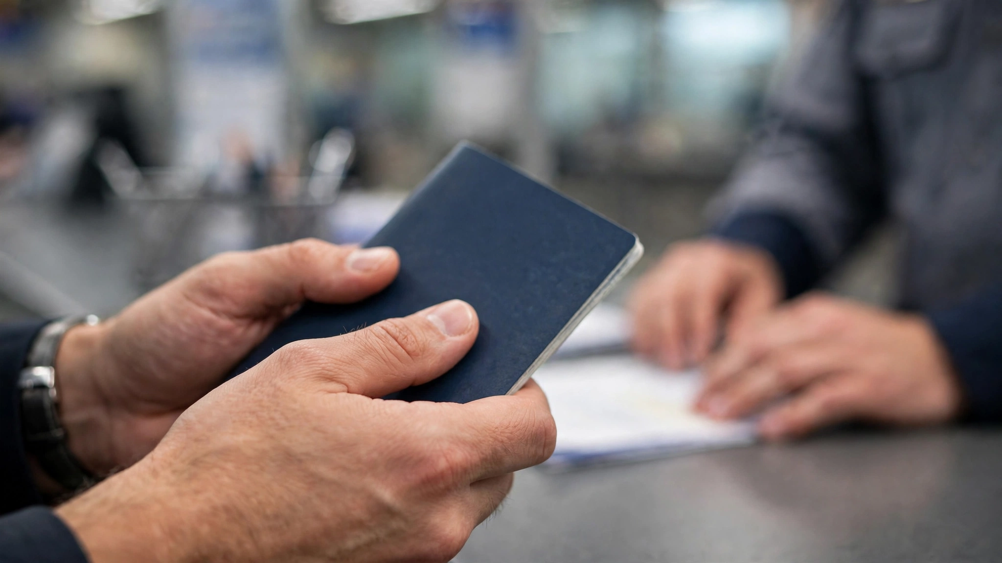 Close-up of hands holding a closed passport at an airport document counter