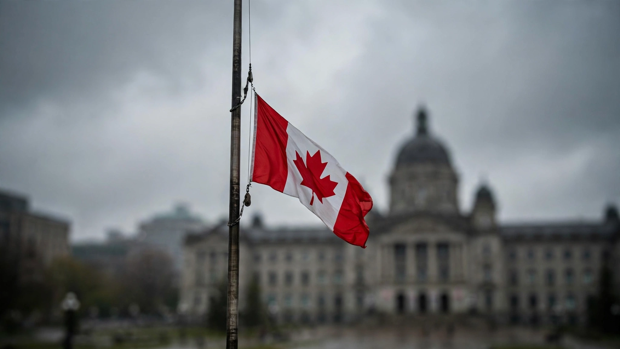 The Canadian national flag flying at half-staff against an overcast sky.