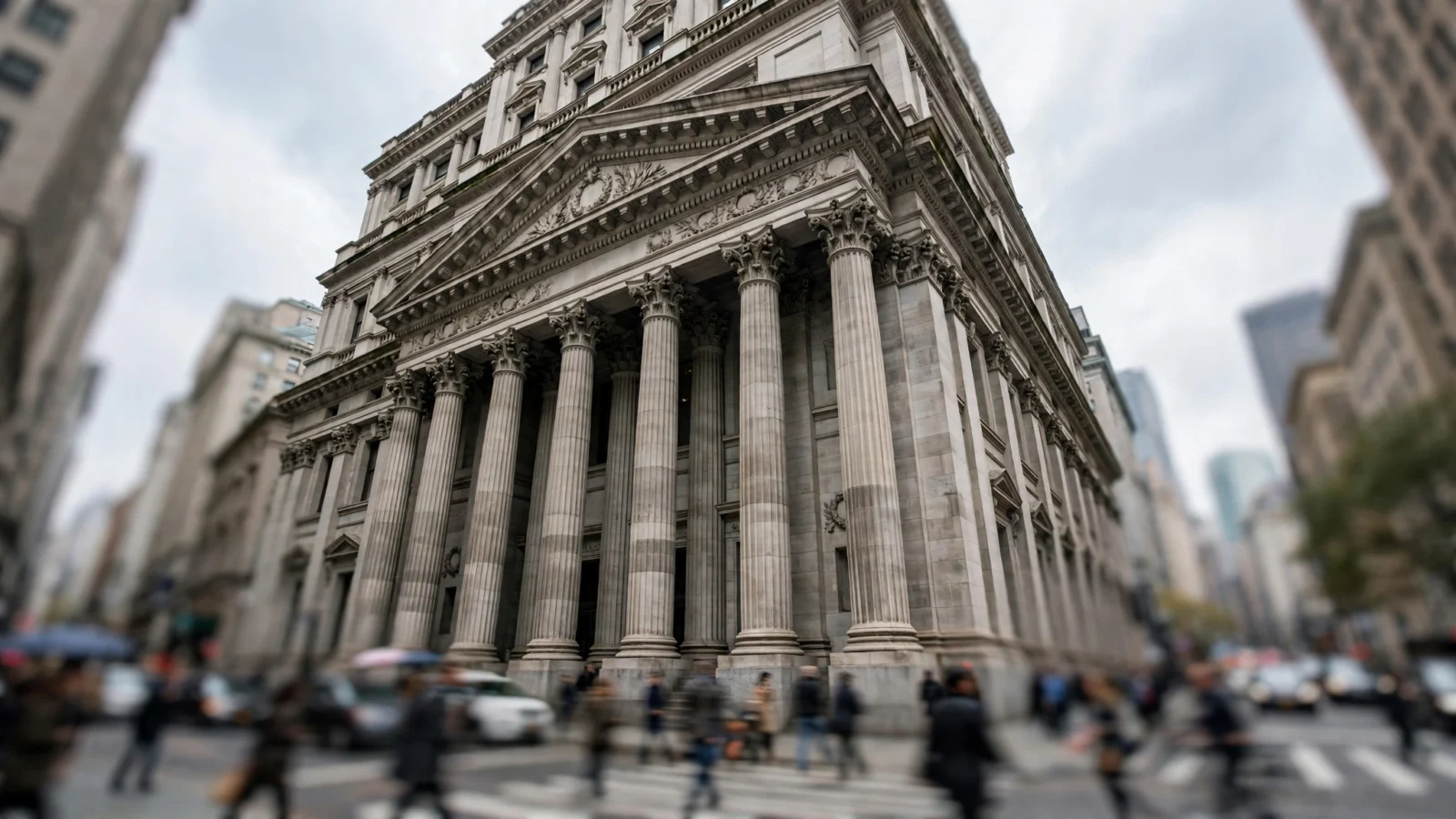 A classical stone financial building facade with tall columns and blurred pedestrians at street level