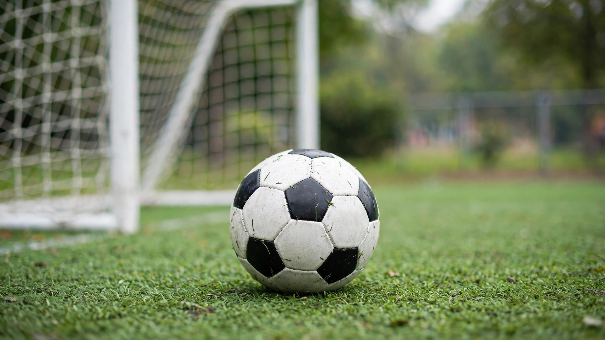 A soccer ball resting on artificial turf in front of a youth soccer goal net
