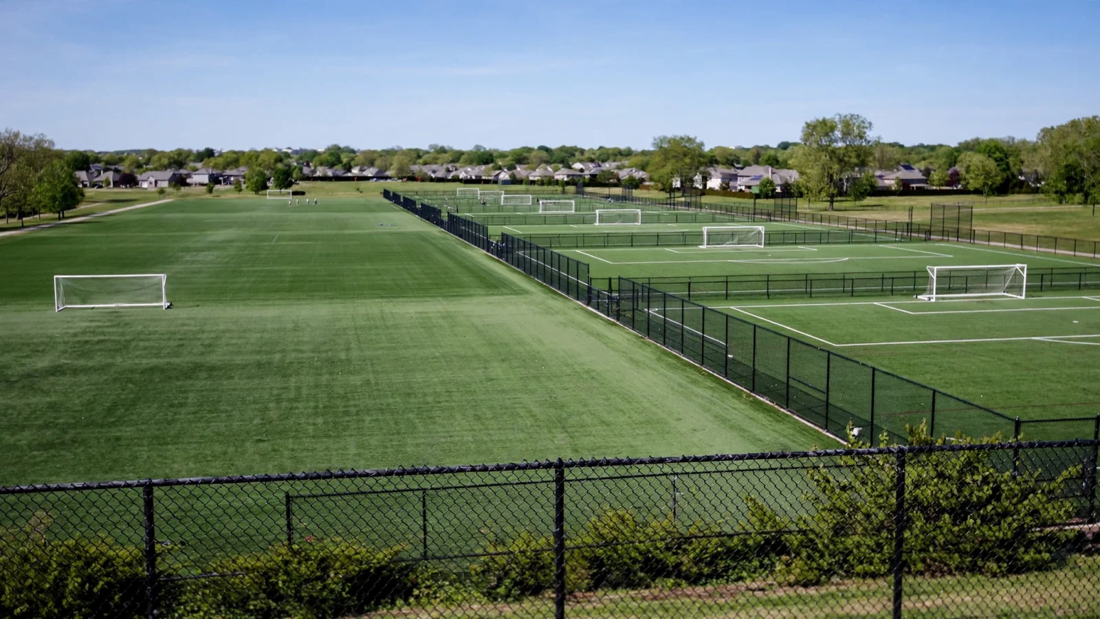 Multiple fenced youth soccer fields with goalposts at a large sports complex on a clear day