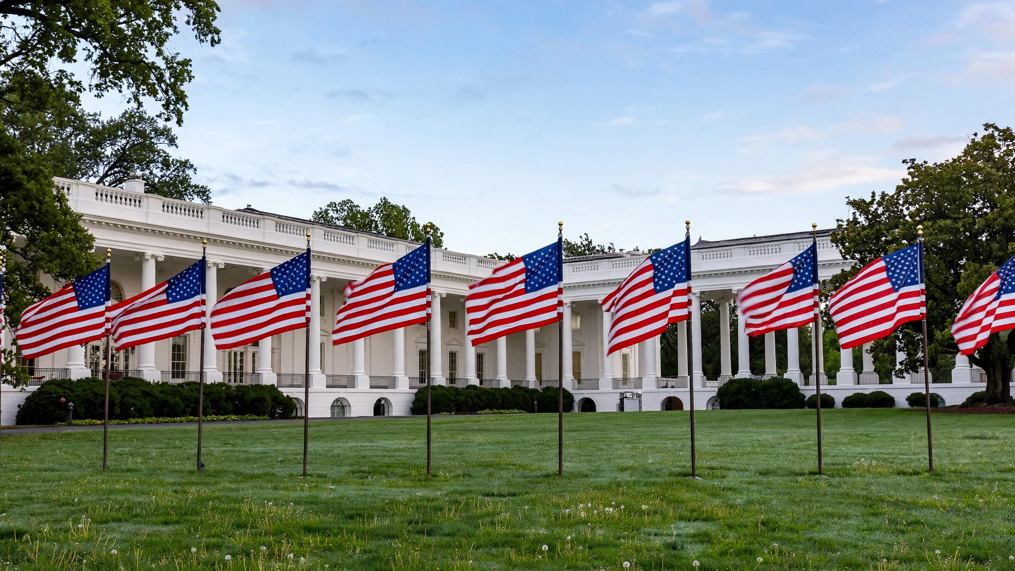 A row of American flags on poles in front of the White House colonnade