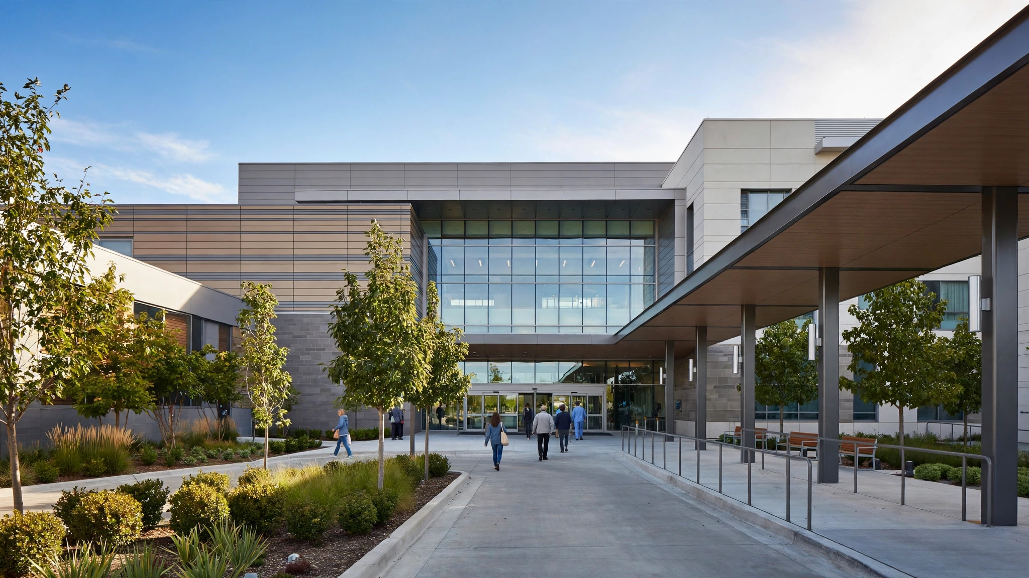 People walk toward the glass entrance of a modern hospital building on a clear day