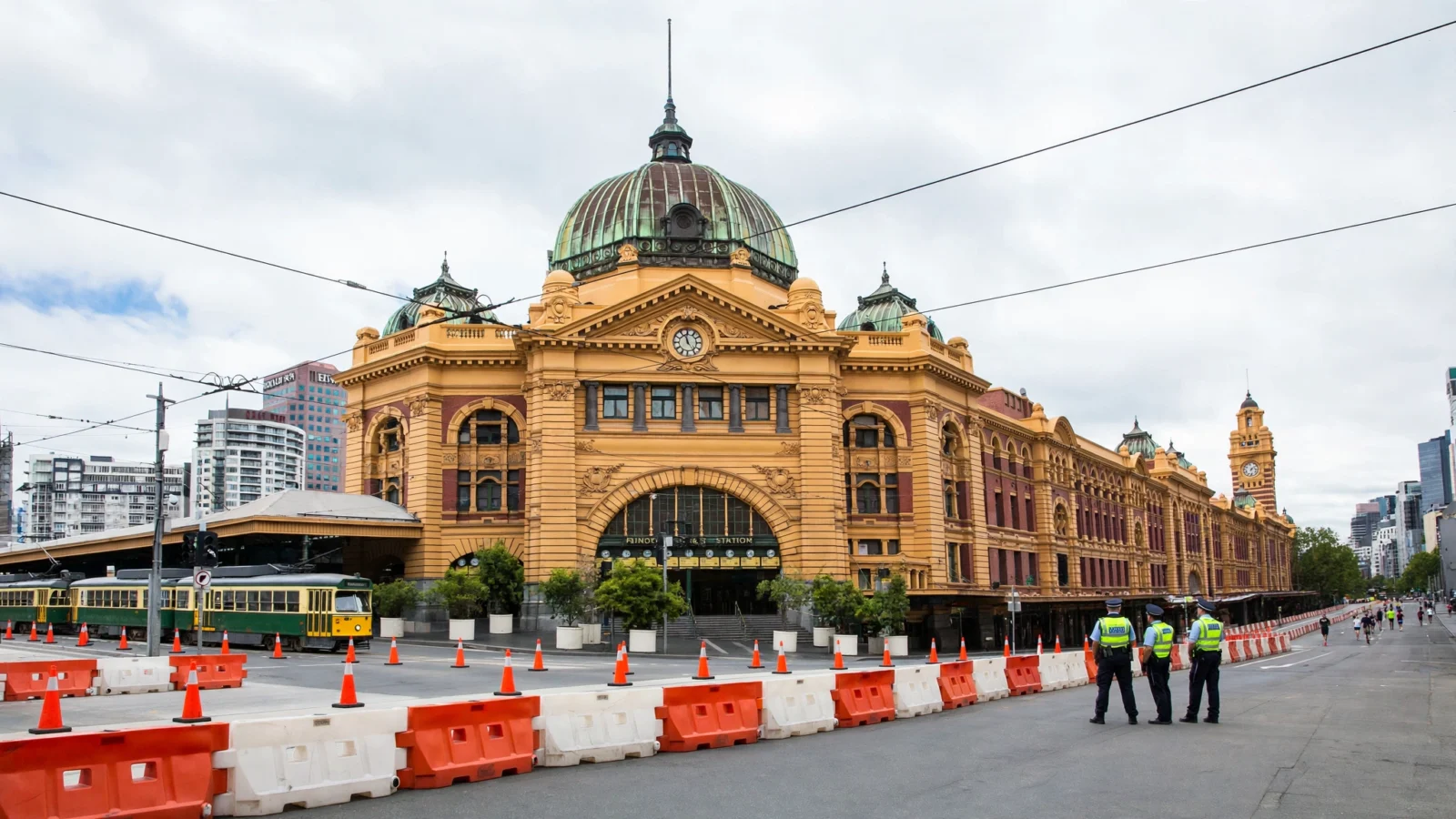Police officers stand beside road barriers on a cordoned-off street near a historic Melbourne railway station during the Melbourne Marathon