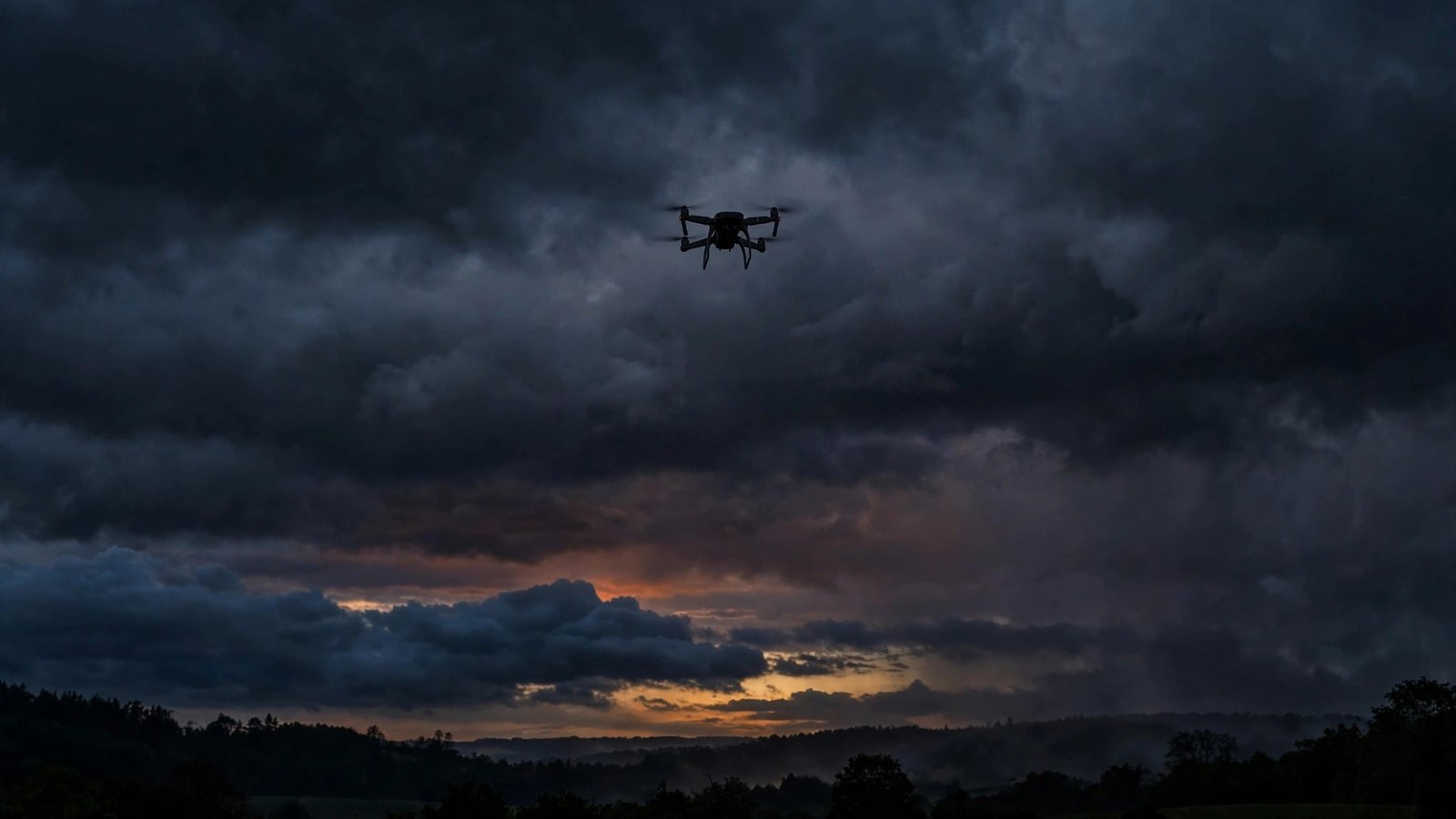 A small quadcopter drone silhouetted against dark storm clouds at dusk.