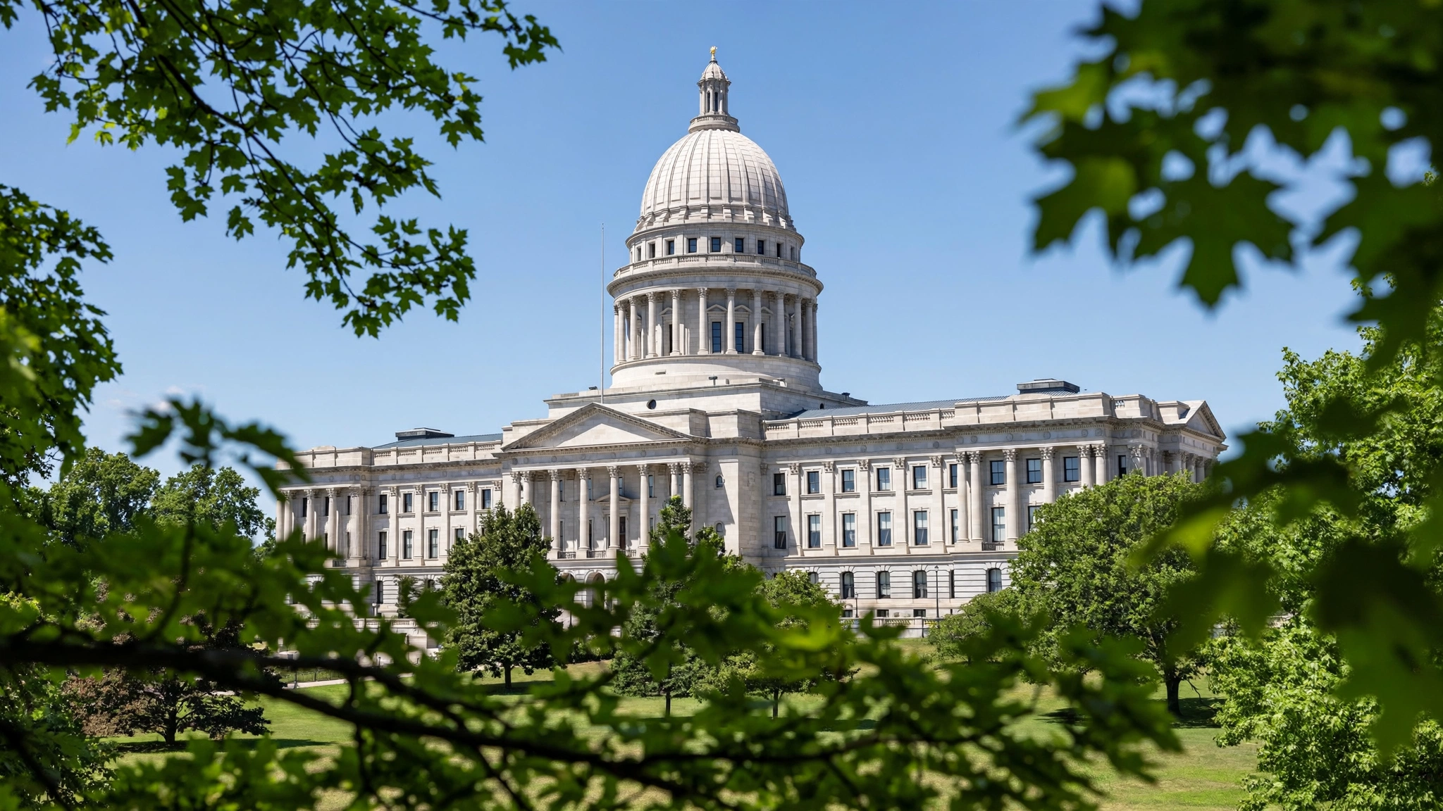 A white-domed state capitol building framed by green trees under a blue sky