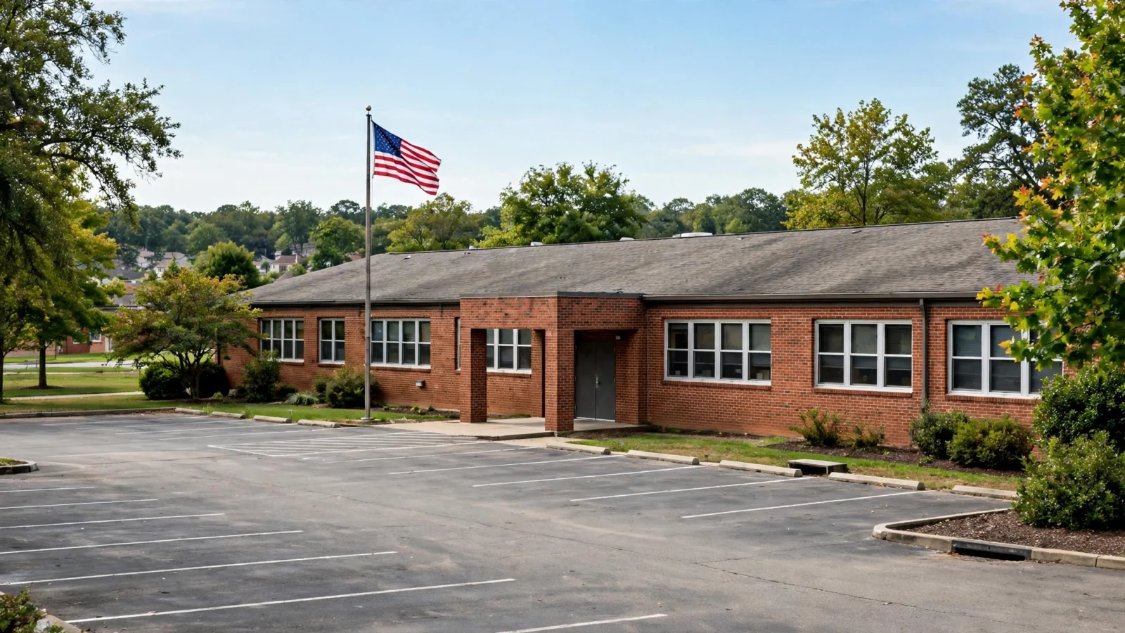 A brick elementary school building with an American flag flying over an empty parking lot