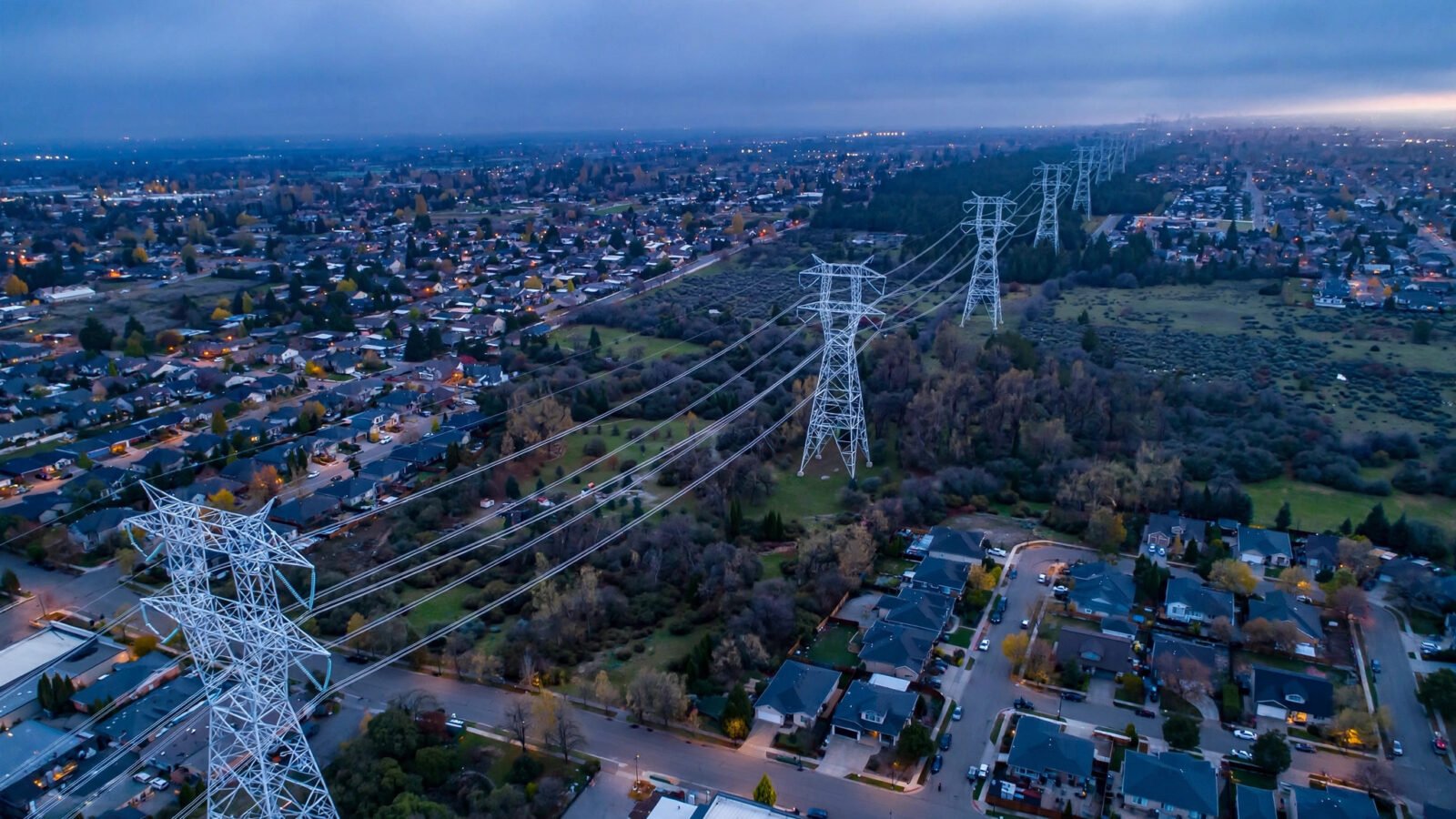 High-voltage transmission towers over a suburban neighborhood at dusk
