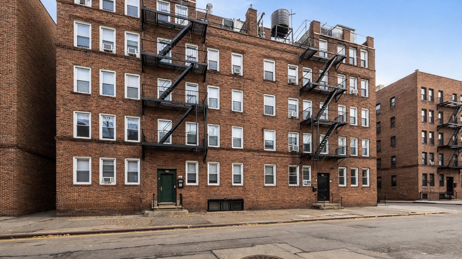 A brick apartment building with metal fire escapes on a New York City street.