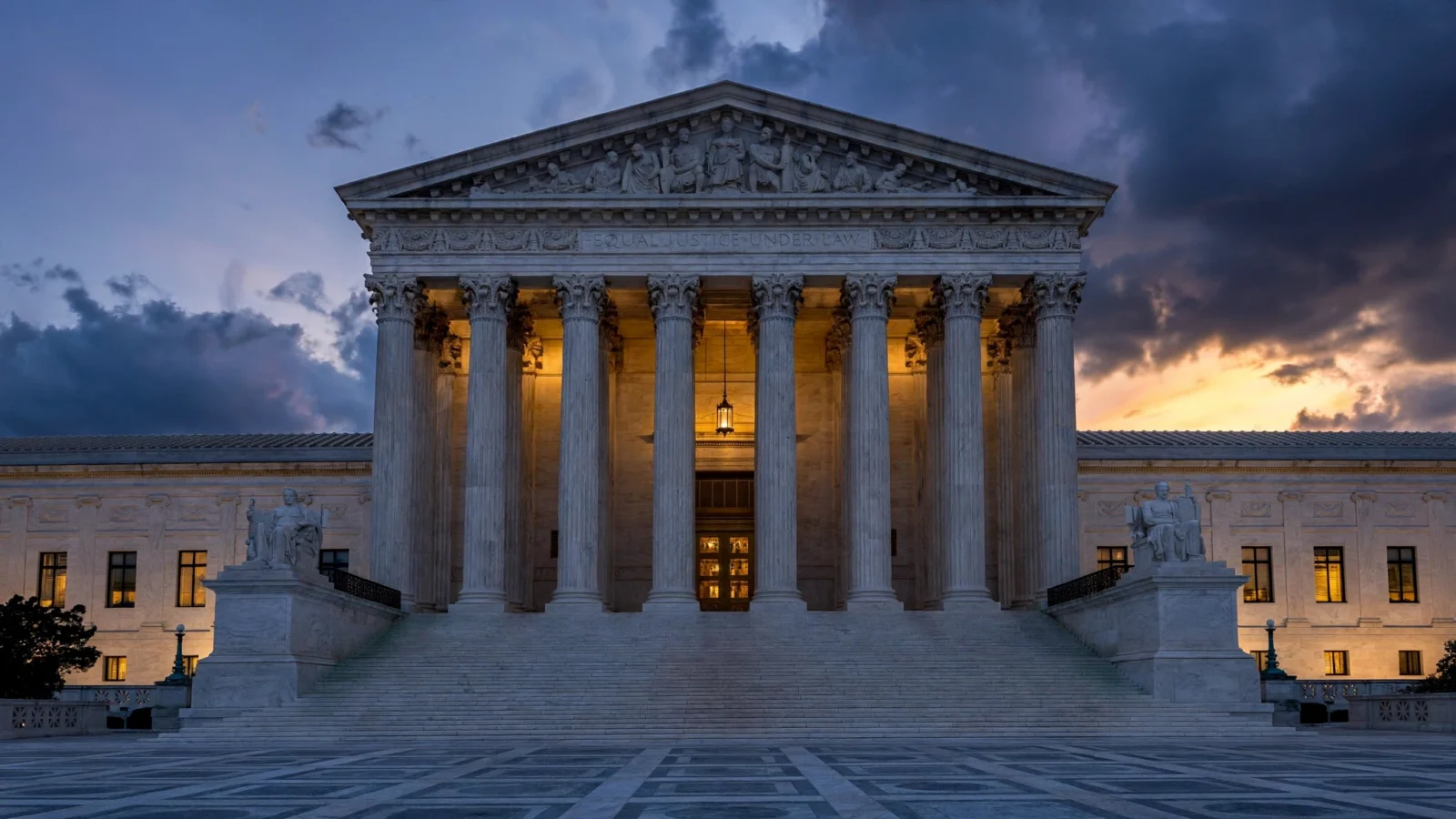 The neoclassical facade of the U.S. Supreme Court building with its columned portico and carved inscription at dusk