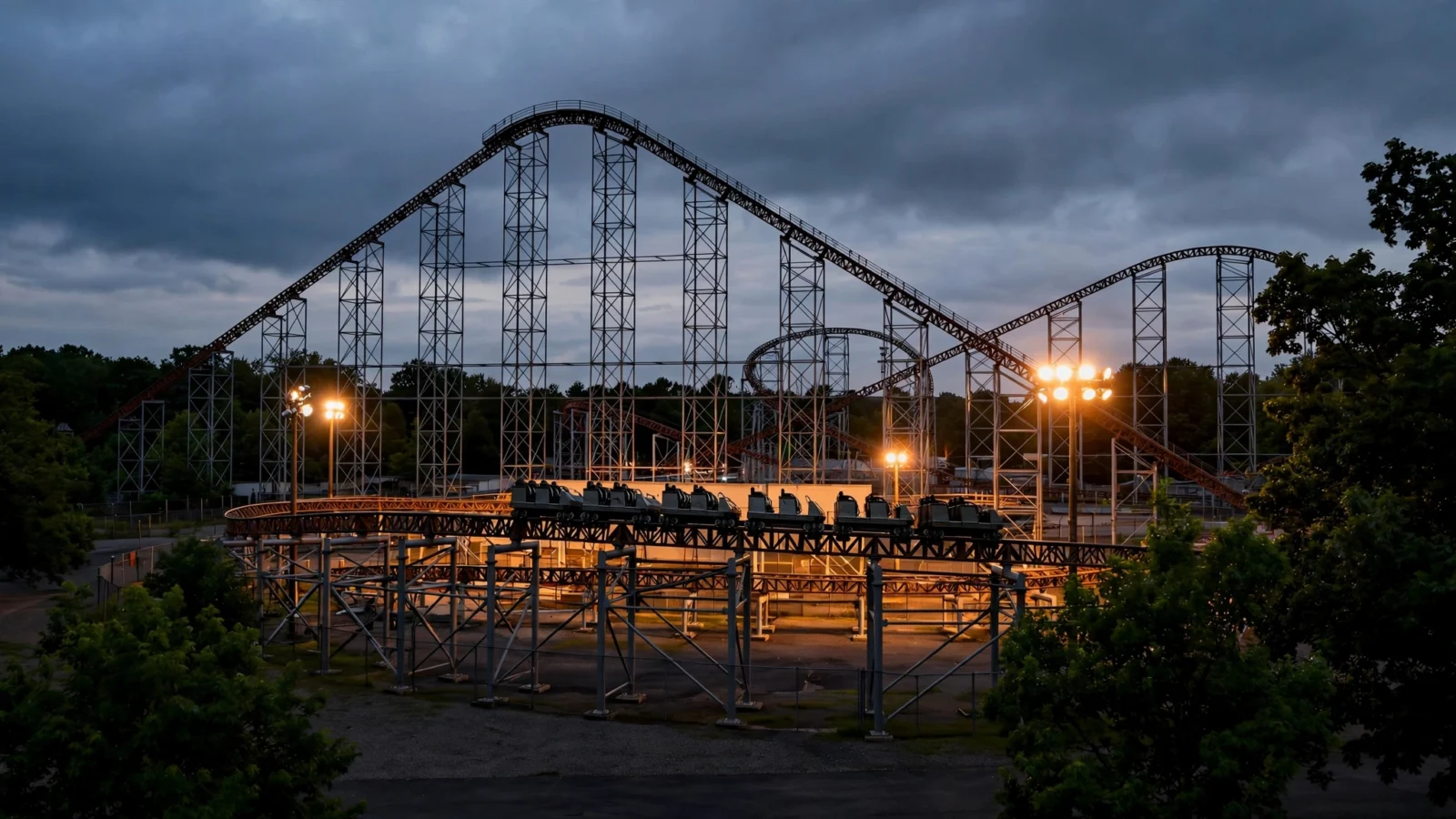 A steel roller coaster silhouette against a cloudy evening sky at an amusement park