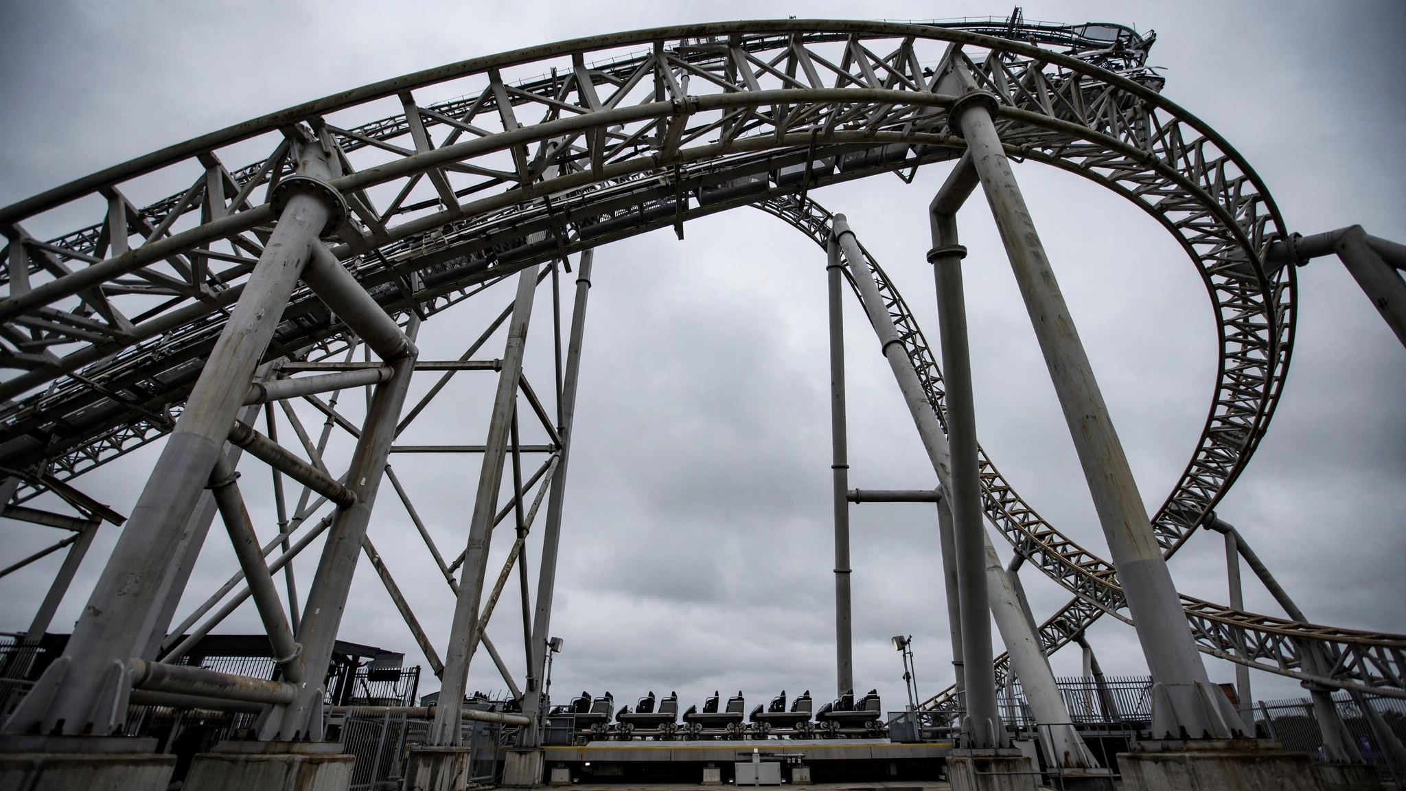 Low-angle view of a steel roller coaster track and support structure under a gray sky