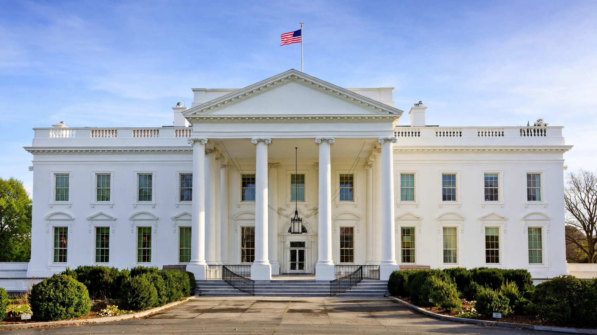 The White House North Portico with an American flag flying from the roof on a clear day.