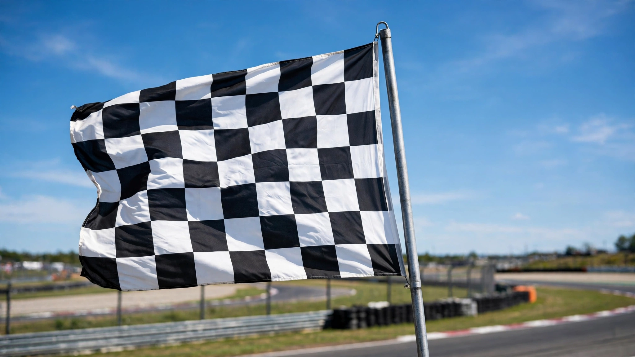A checkered flag waving on a pole against a blue sky at a racetrack