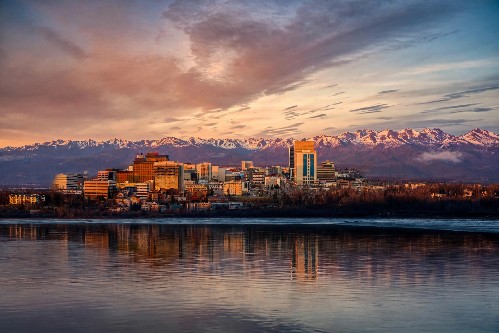 The downtown Anchorage skyline at sunset with snow-capped mountains behind it