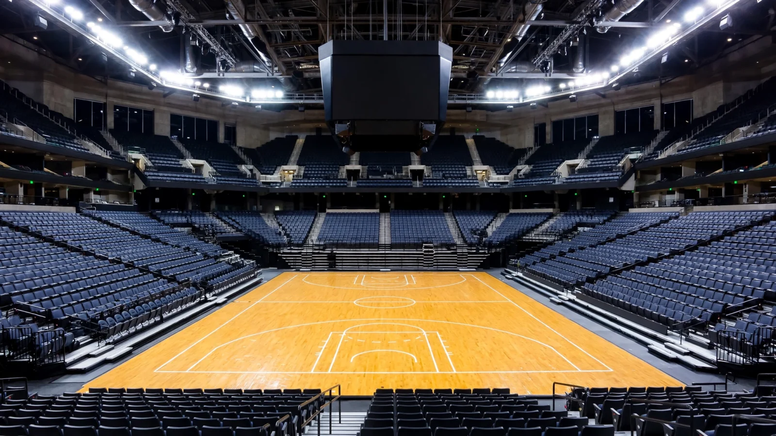 An empty professional basketball arena at night with the court lit by spotlights